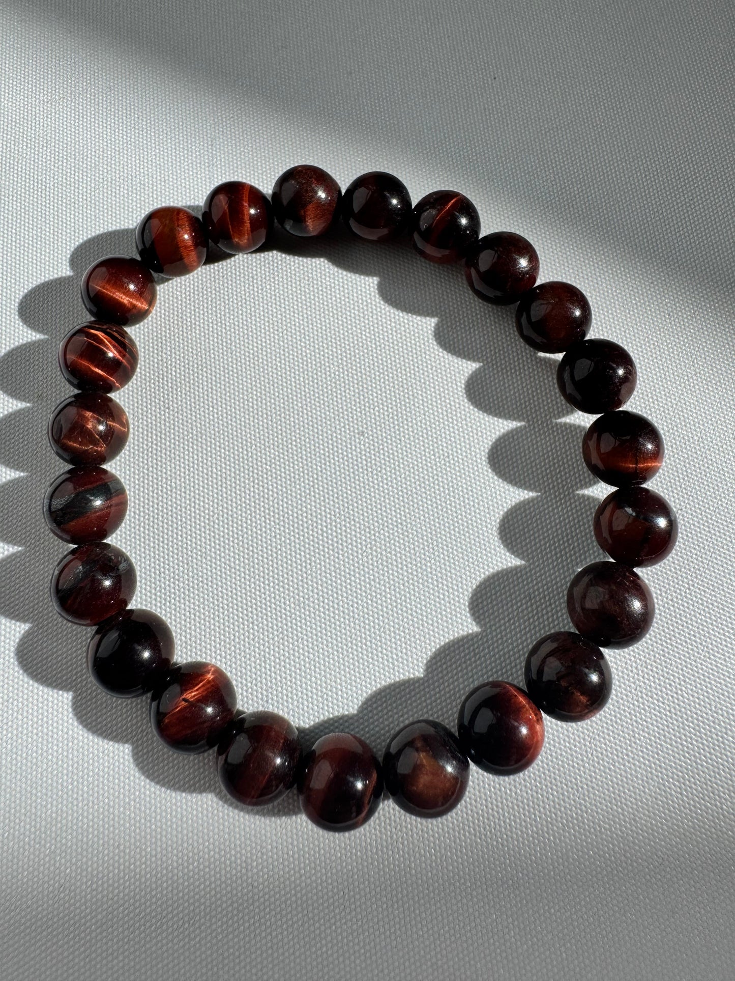 Red Tigers Eye Crystal Bracelet featuring glossy, dark red beads arranged in a circle, ideal for grounding energy and boosting confidence.