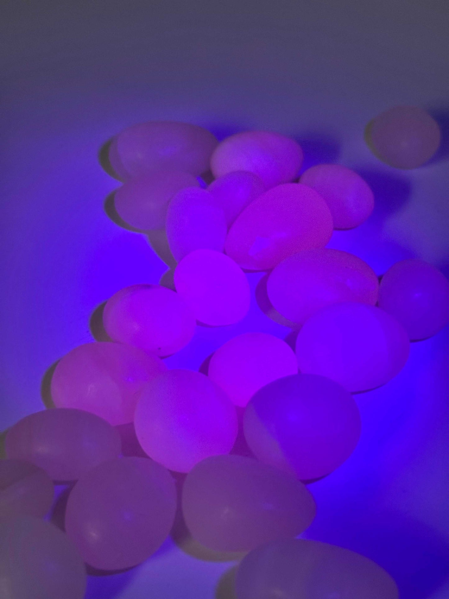 Pink Mangano Calcite Tumble Stones glowing under UV light, highlighting their vibrant fluorescence and appeal for bespoke crystal collections.