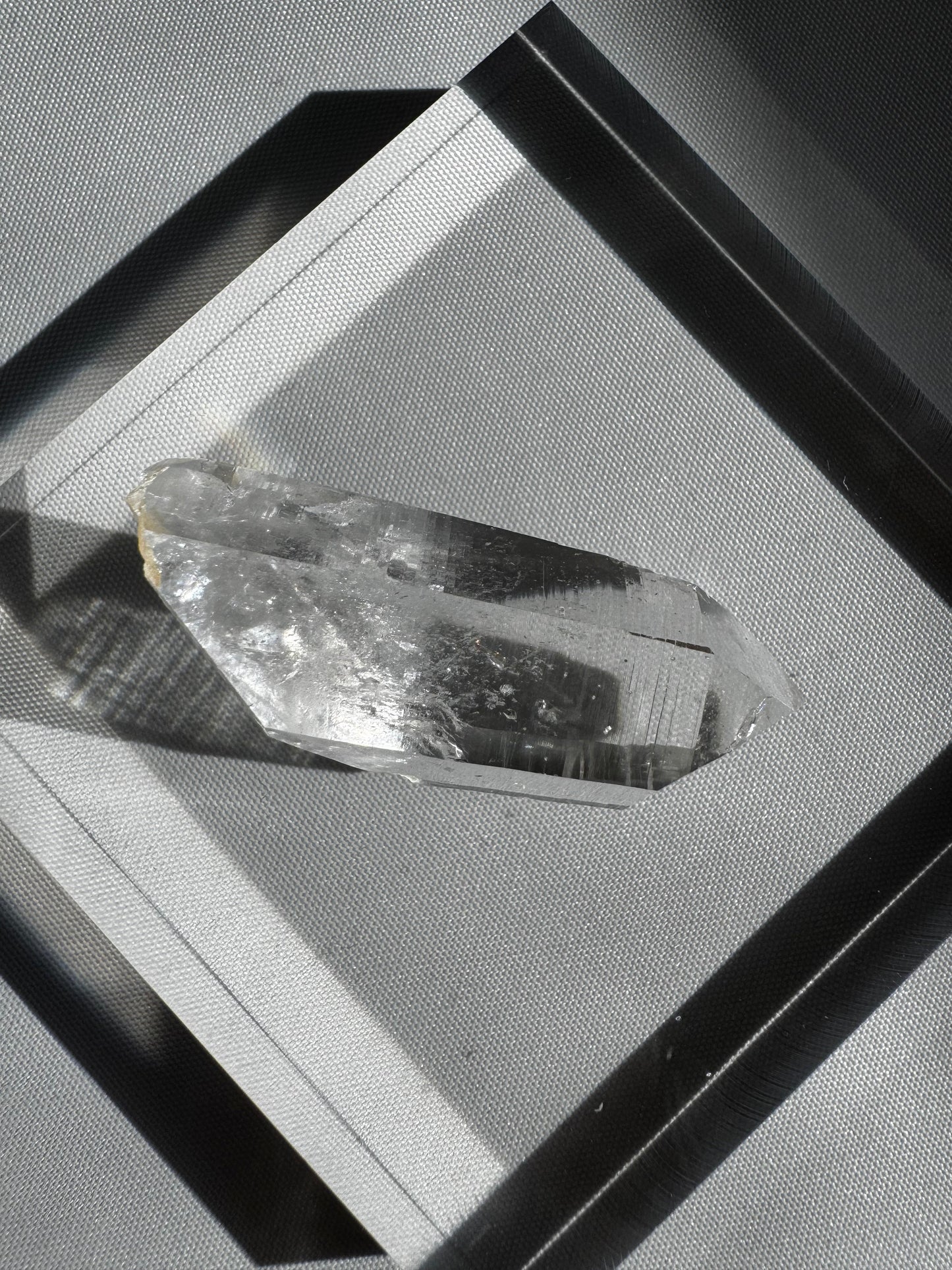Silver Light Crystal Lemurian Seed Point DT gemstone with high clarity and striations, displayed on a geometric silver background.