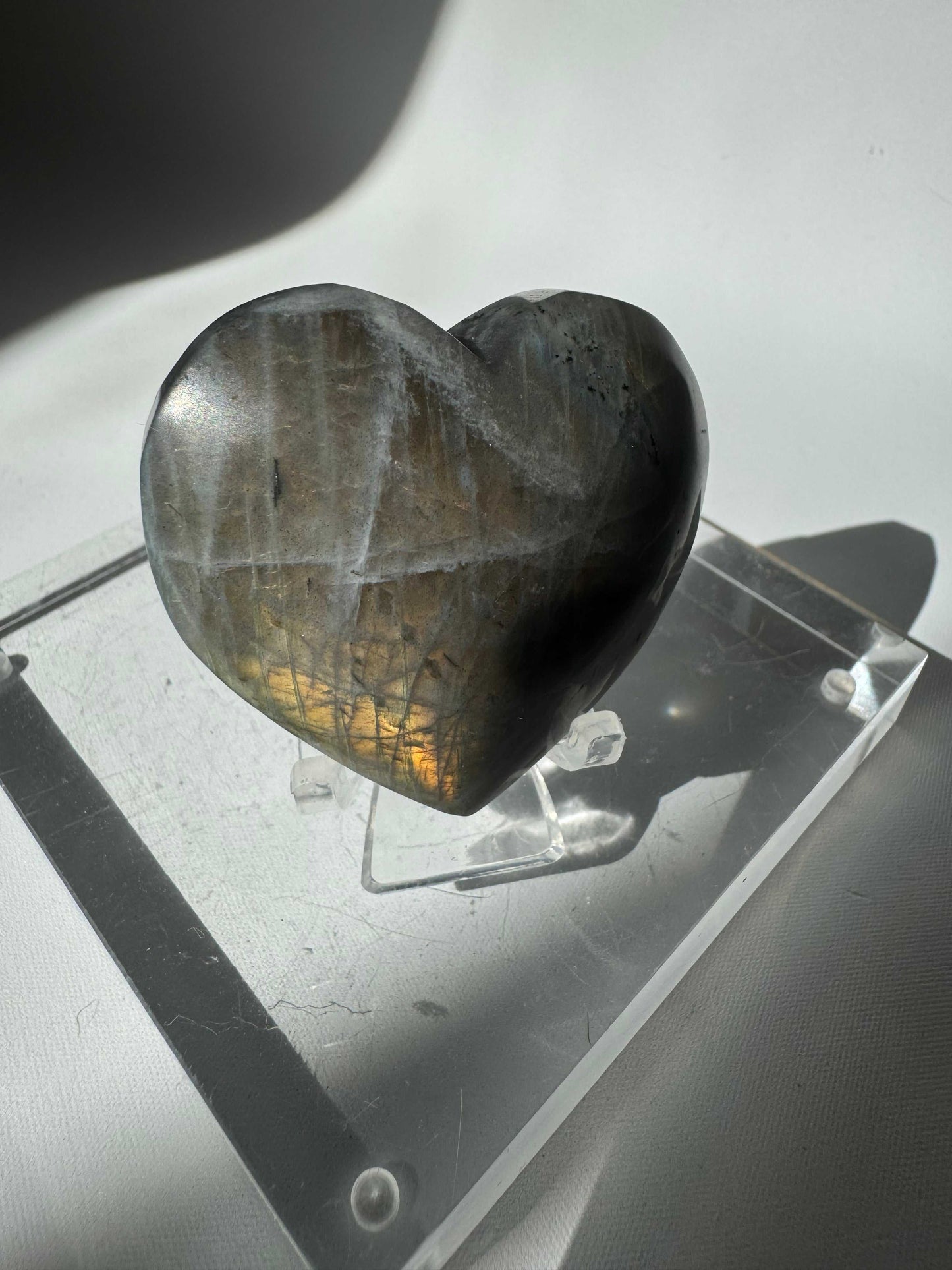 Labradorite Puffy Heart #4 from Bespoke Crystals displayed on a clear acrylic stand, showcasing its iridescent sheen and heart-shaped polish.