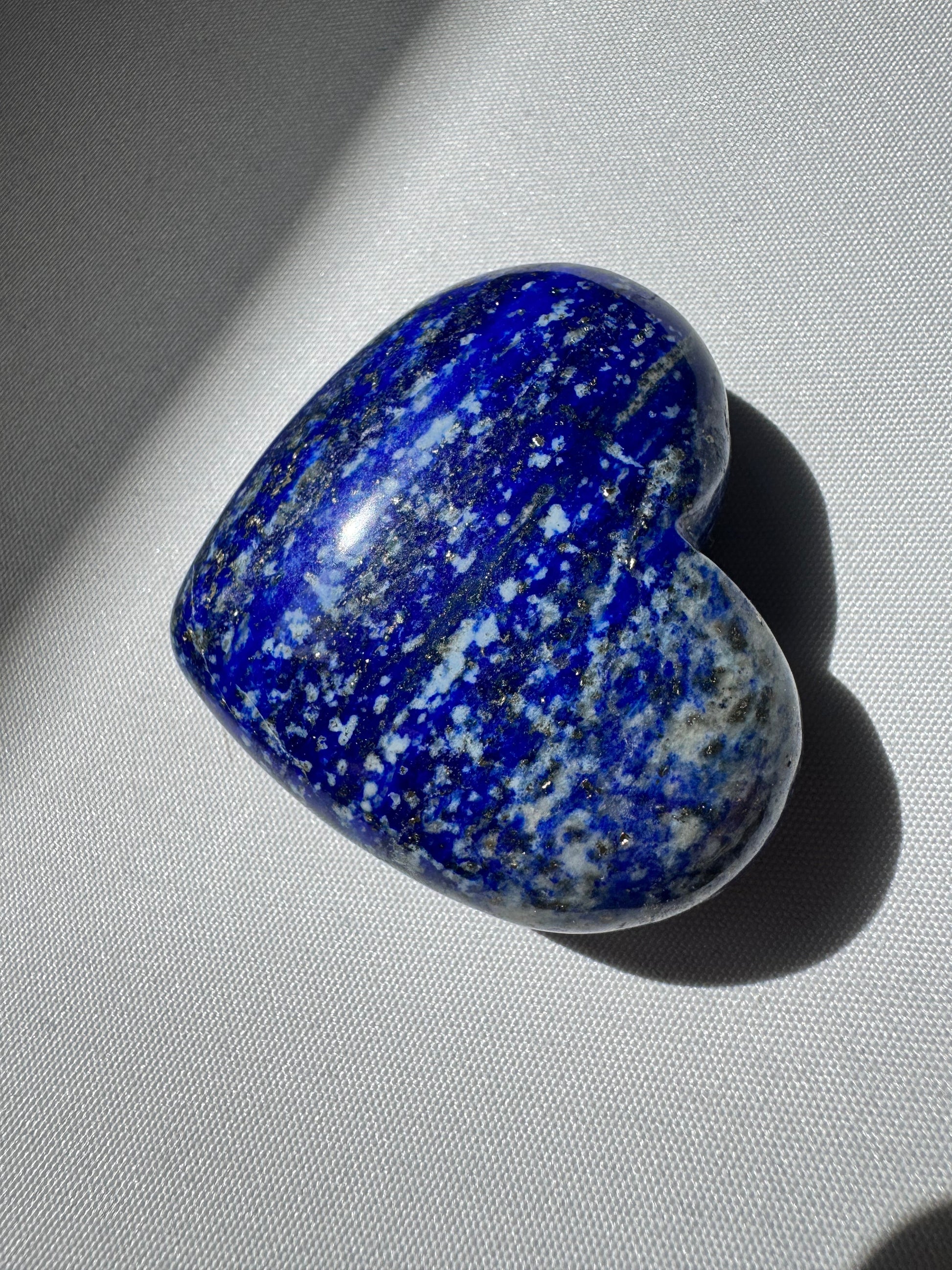 Polished Lapis Lazuli Heart | Bespoke Crystals with vivid azure tones and natural mineral patterns, resting on white fabric under natural light.
