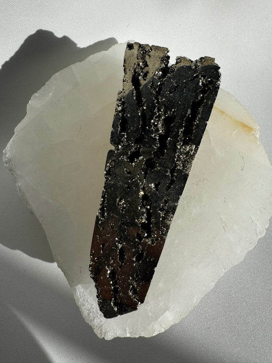 Pyrite Crystal Obelisk #2 with shimmering gold-black surface displayed on a white quartz base, ideal for crystal decor and energy work.