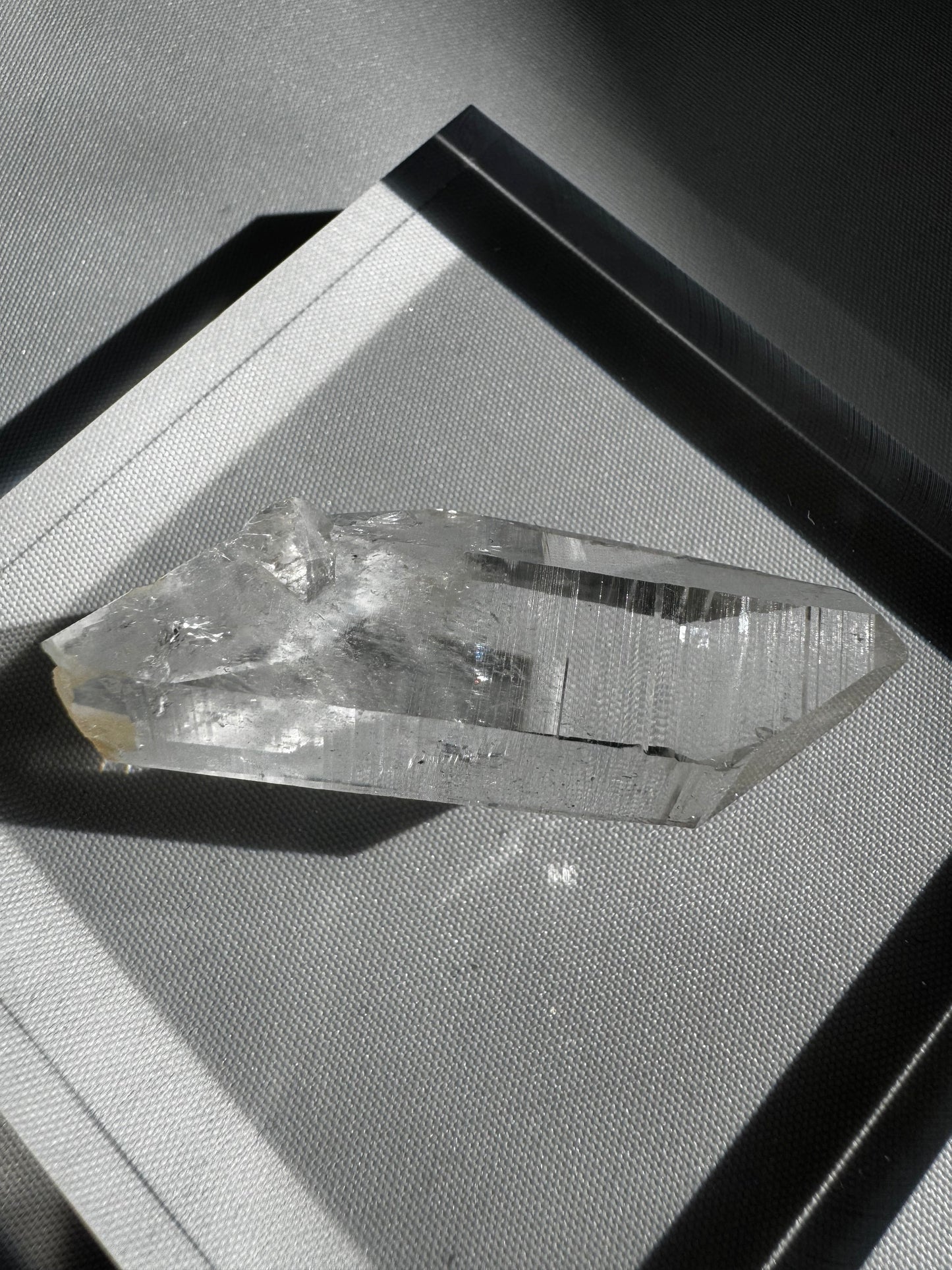 Silver Light Crystal Lemurian Seed Point DT with high clarity and horizontal striations, displayed on a textured surface under natural light.