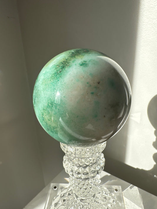 Green Flower Agate Crystal Sphere #2 with soft green and white hues, displayed on a clear ornate stand. Ideal for collectors and crystal healing.
