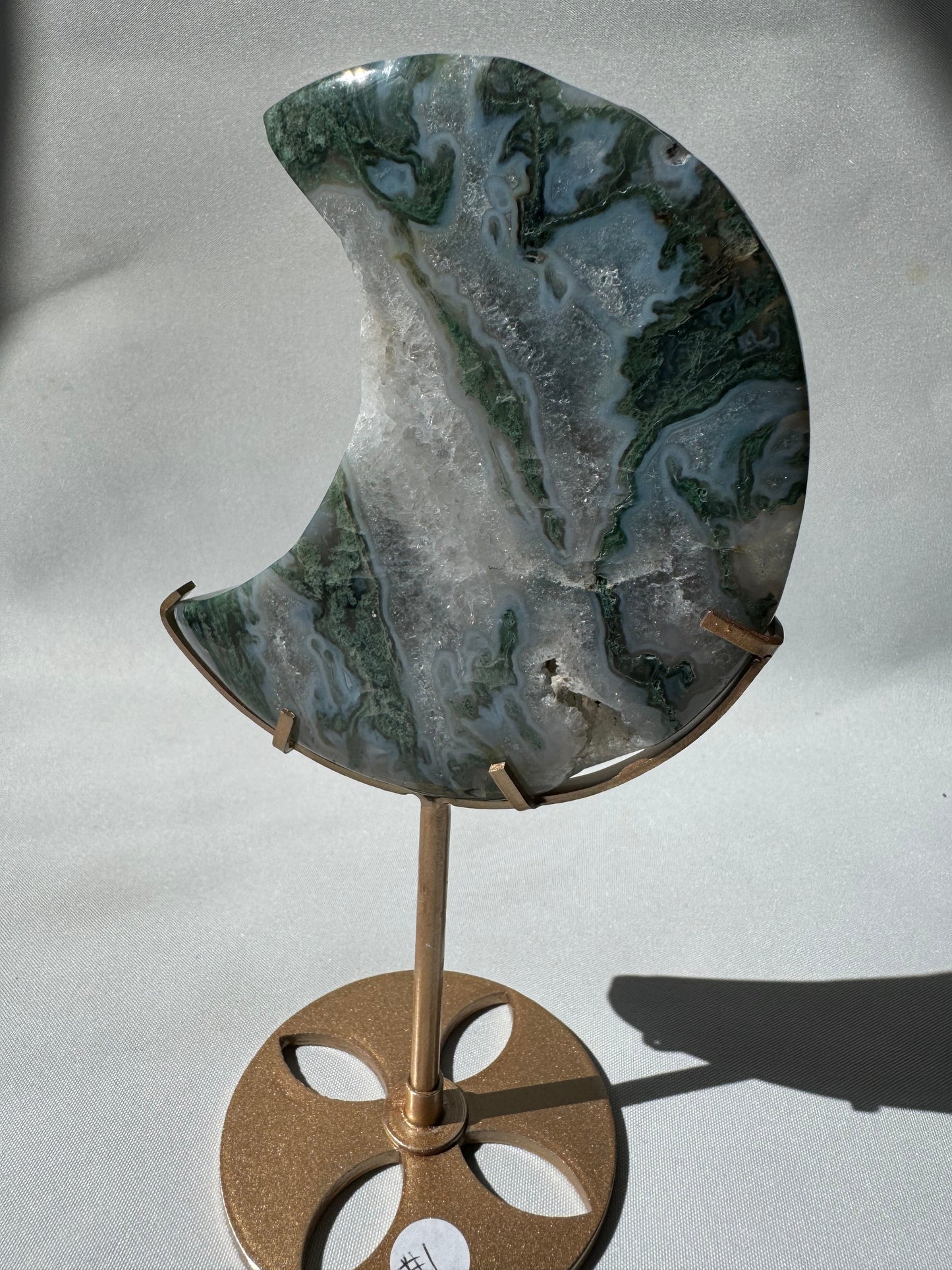 Moss Agate Crystal Moon on Stand #1 featuring lush green inclusions and druzy texture, mounted on a gold display stand for elegant decor.