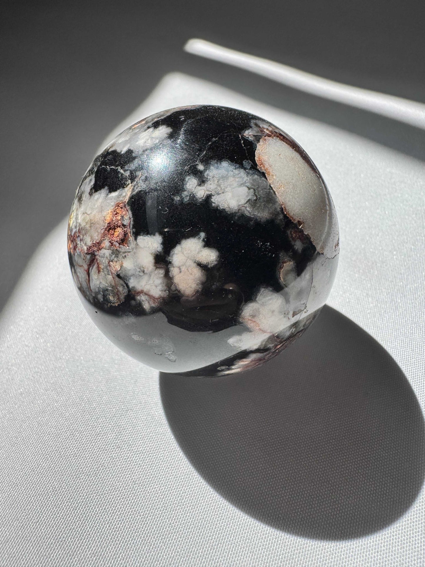 Polished Black Flower Agate Sphere showcasing white blossom-like inclusions, perfect for spiritual growth and home decor.