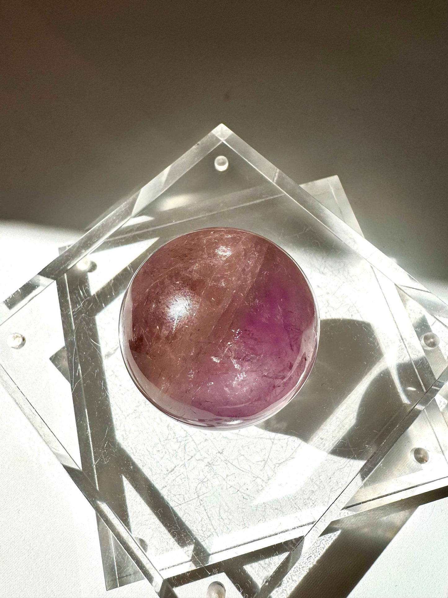Ametrine Crystal Sphere #1 | Bespoke Crystals featuring a fusion of purple and golden hues, displayed on a clear acrylic stand under natural light.