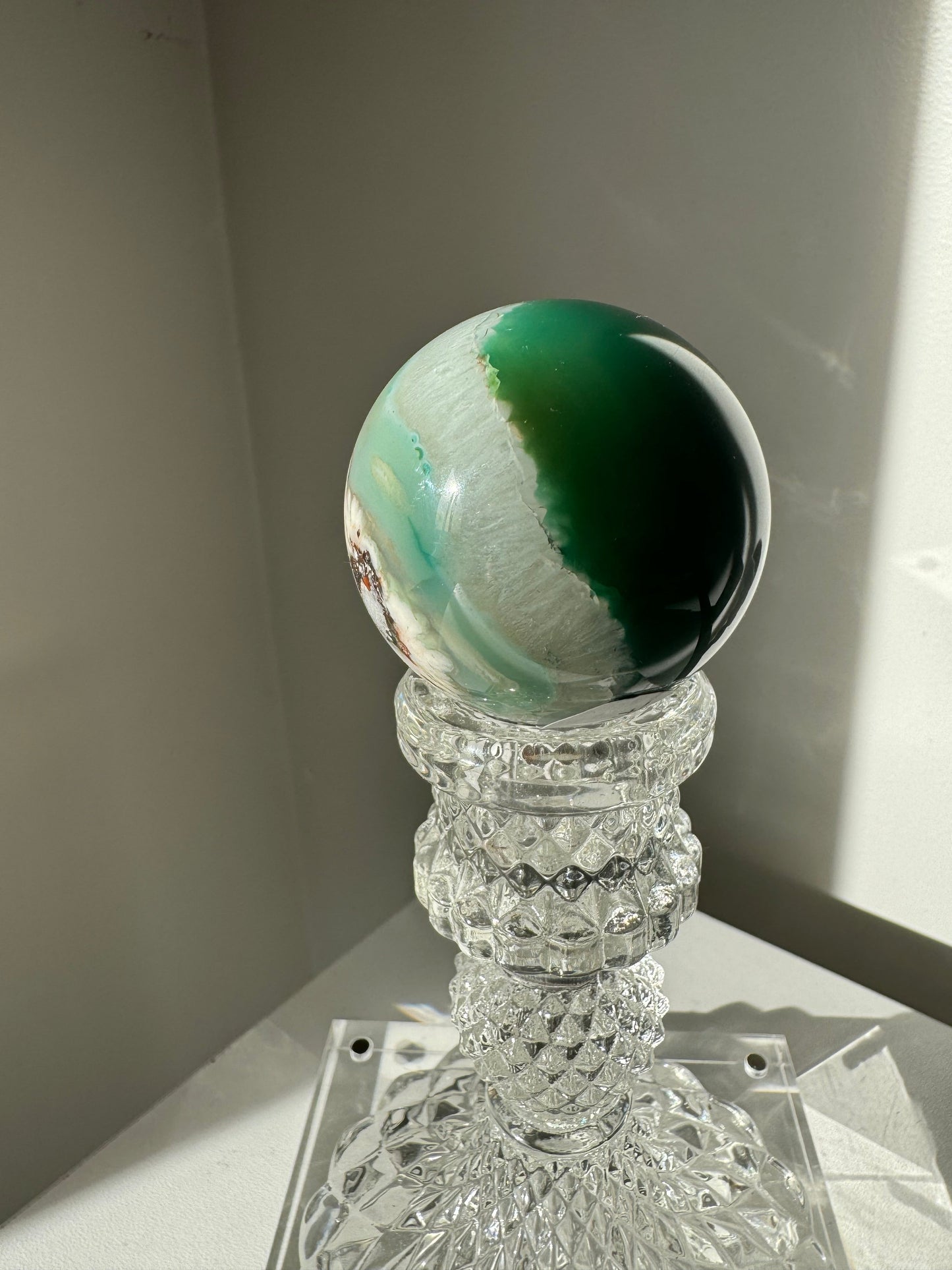 Side view of Green Flower Agate Crystal Sphere #4 showing layered green and white banding, placed on an ornate crystal pedestal.