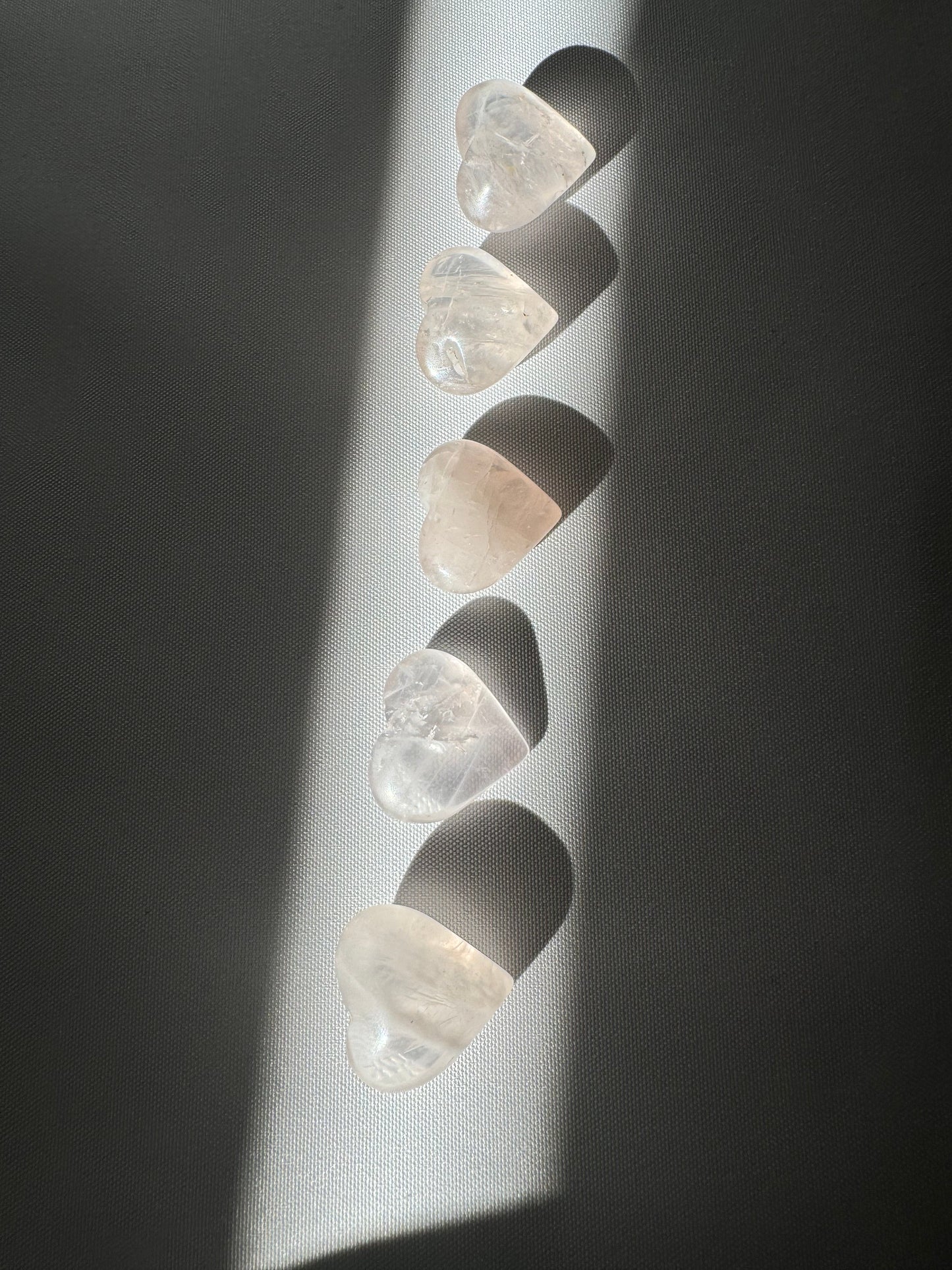 Mini Rose Quartz Crystal Hearts | Bespoke Crystals arranged vertically in a beam of sunlight, showcasing their soft pink hue and polished finish.