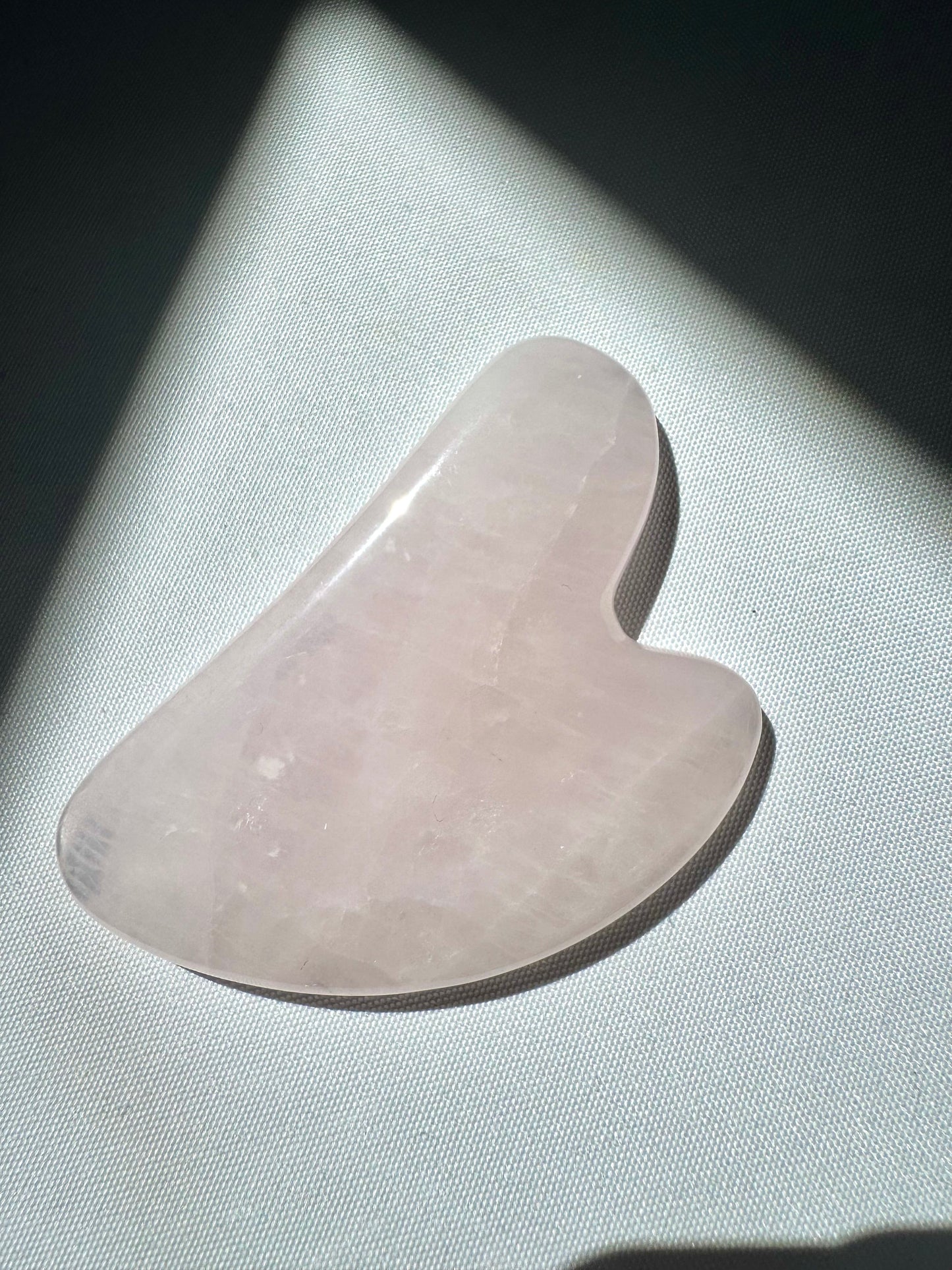 Close-up of Rose Quartz Crystal Gua Sha from Bespoke Crystals under natural light, highlighting its polished finish and heart-shaped design.