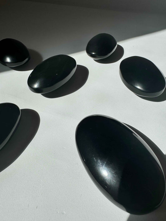 Set of polished Rainbow Obsidian Crystal Palm Stones arranged on a white surface, ideal for grounding and transformation rituals.