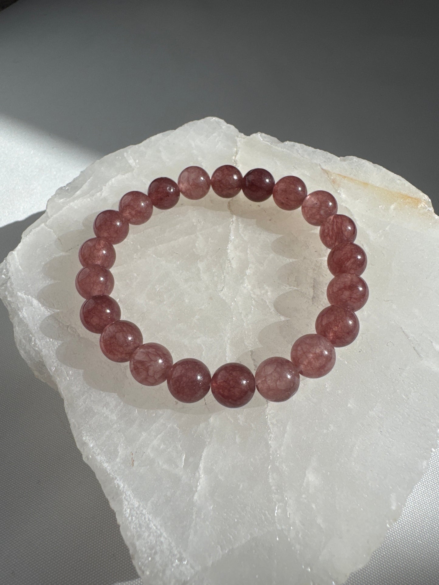 Strawberry Quartz Crystal Bracelet with round pink-red beads on a white quartz slab, ideal for love and spiritual growth jewelry collections.