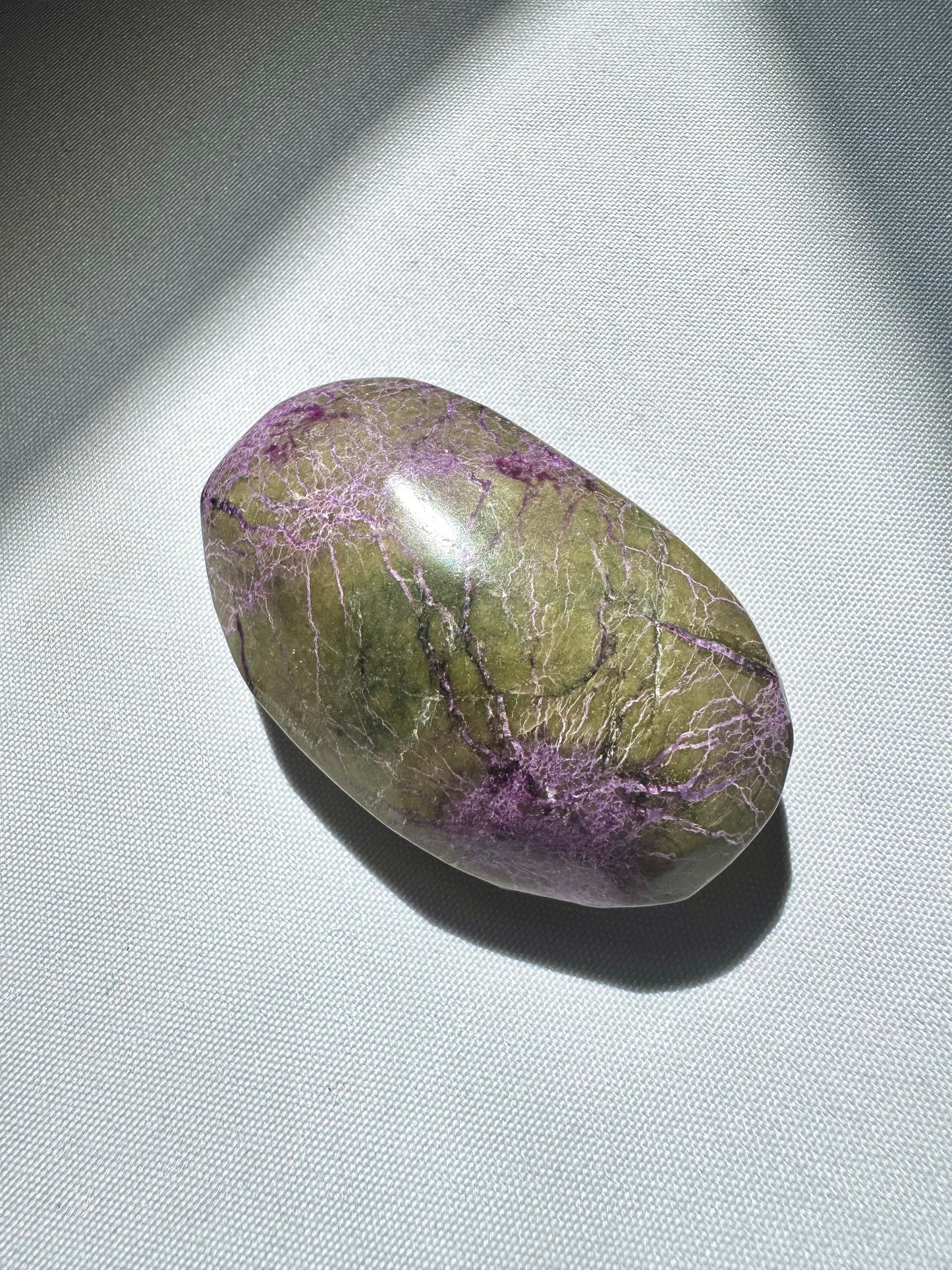 Oval-shaped Atlantisite Crystal Palm Stone showcasing natural green and purple marbling, used for spiritual connection and transformation.