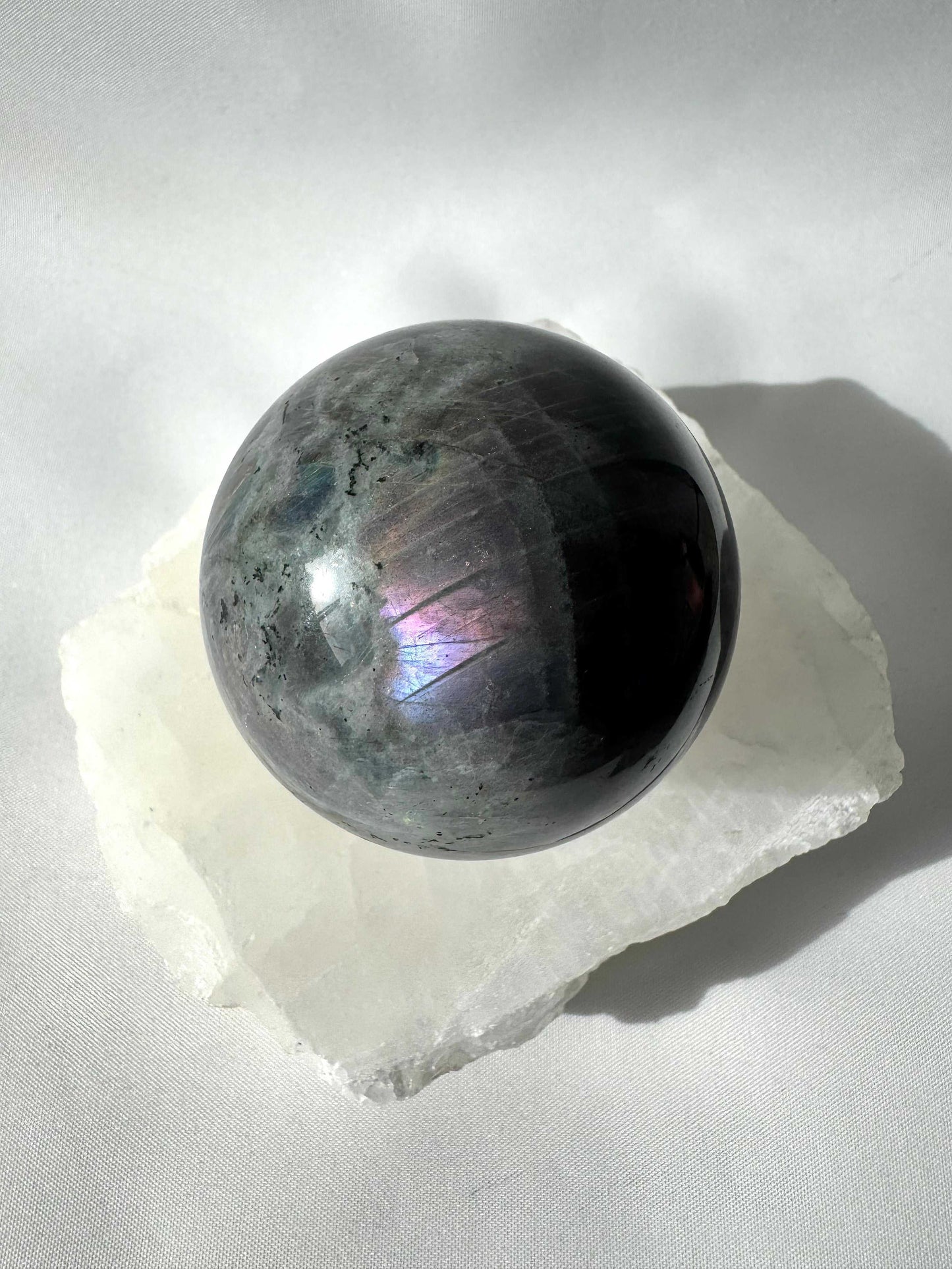 Polished Labradorite Crystal Sphere #3 Bespoke Crystals showing iridescent flash on a white stone base, ideal for crystal enthusiasts and collectors.