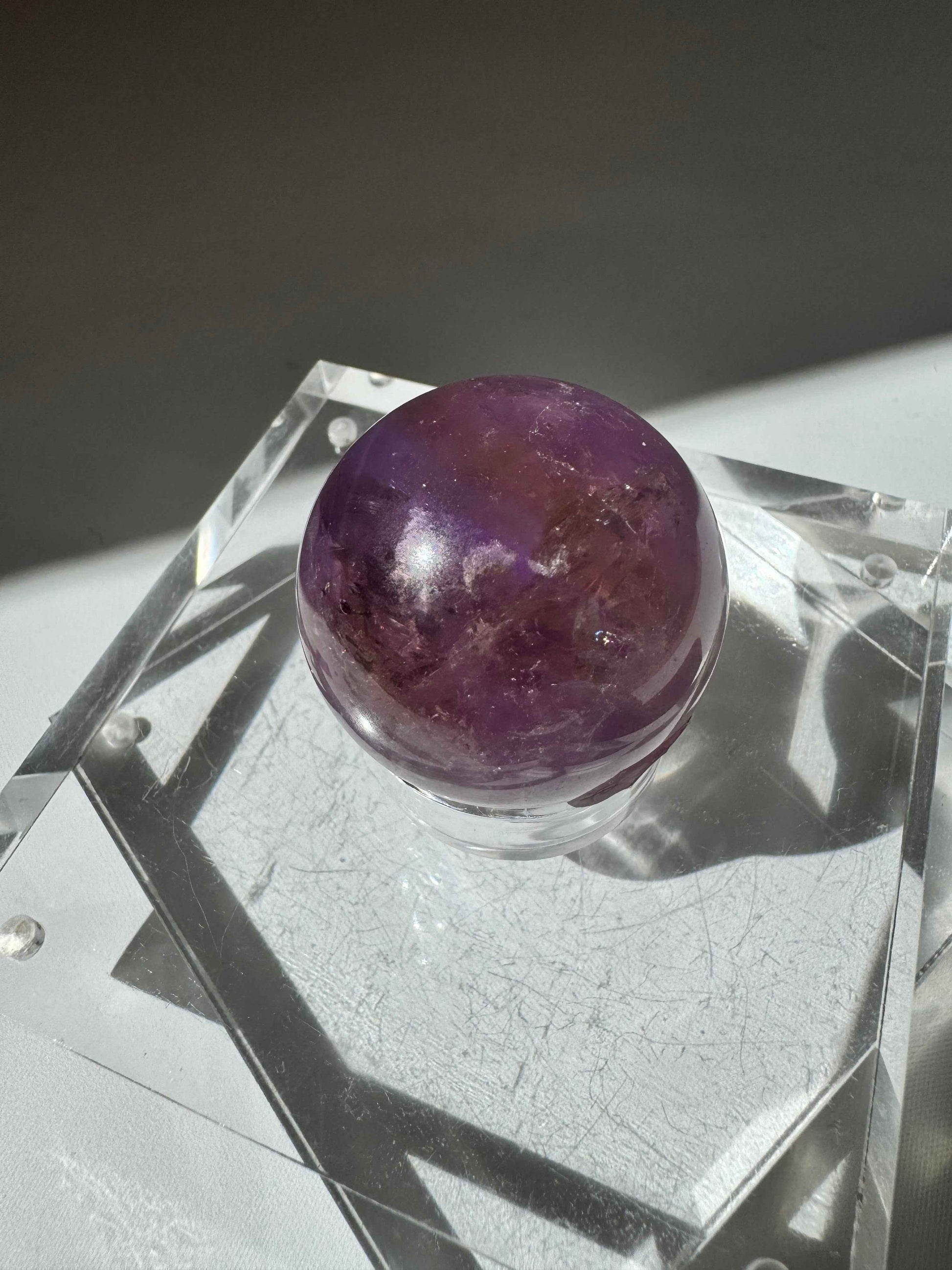 Ametrine Crystal Sphere #2 showcasing a blend of purple and golden hues, displayed on a clear acrylic stand. Ideal for collectors of bespoke crystals.