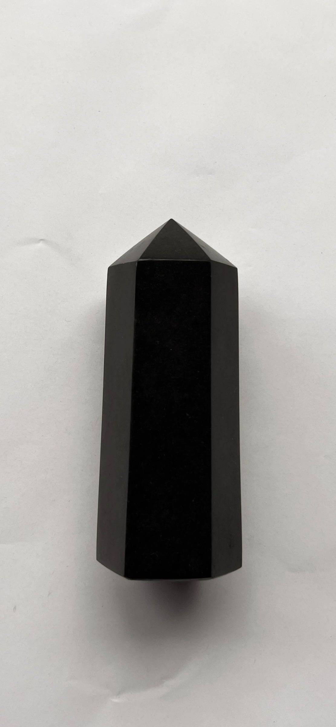 Polished Black Tourmaline Tower crystal lying flat, showcasing its smooth surface and pointed top. Used in energy healing and spiritual protection.