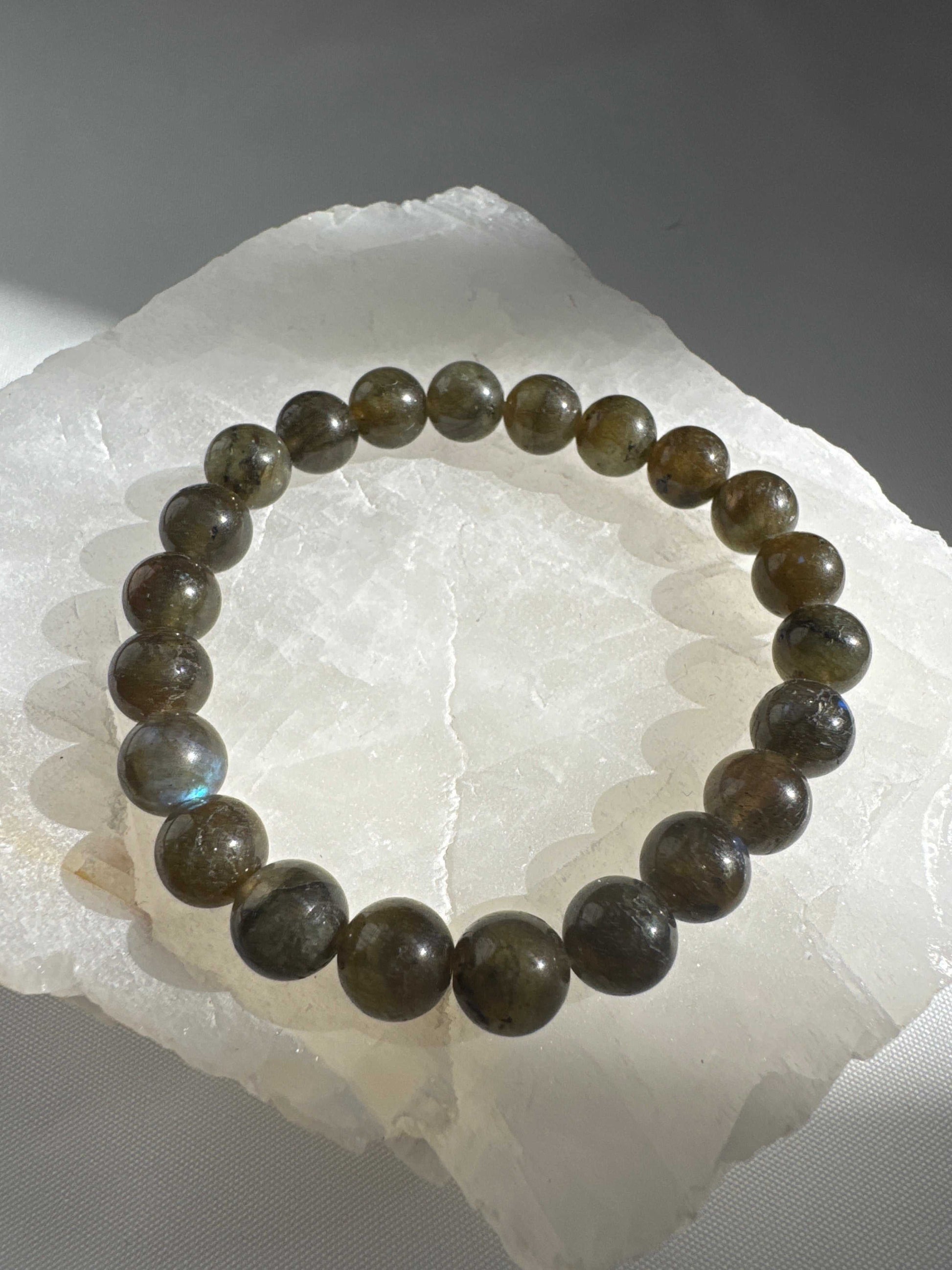 Labradorite Bracelet - Spiritual Protector resting on a white selenite slab, showcasing its natural shimmer and grounding energy properties.