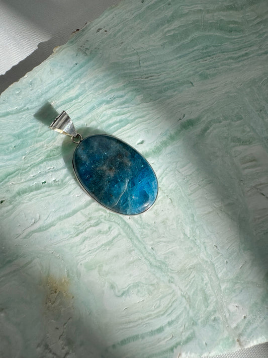 Blue Apatite Crystal Sterling Silver Pendant with oval cut gemstone on textured green stone background, ideal for spiritual and fashion jewelry.