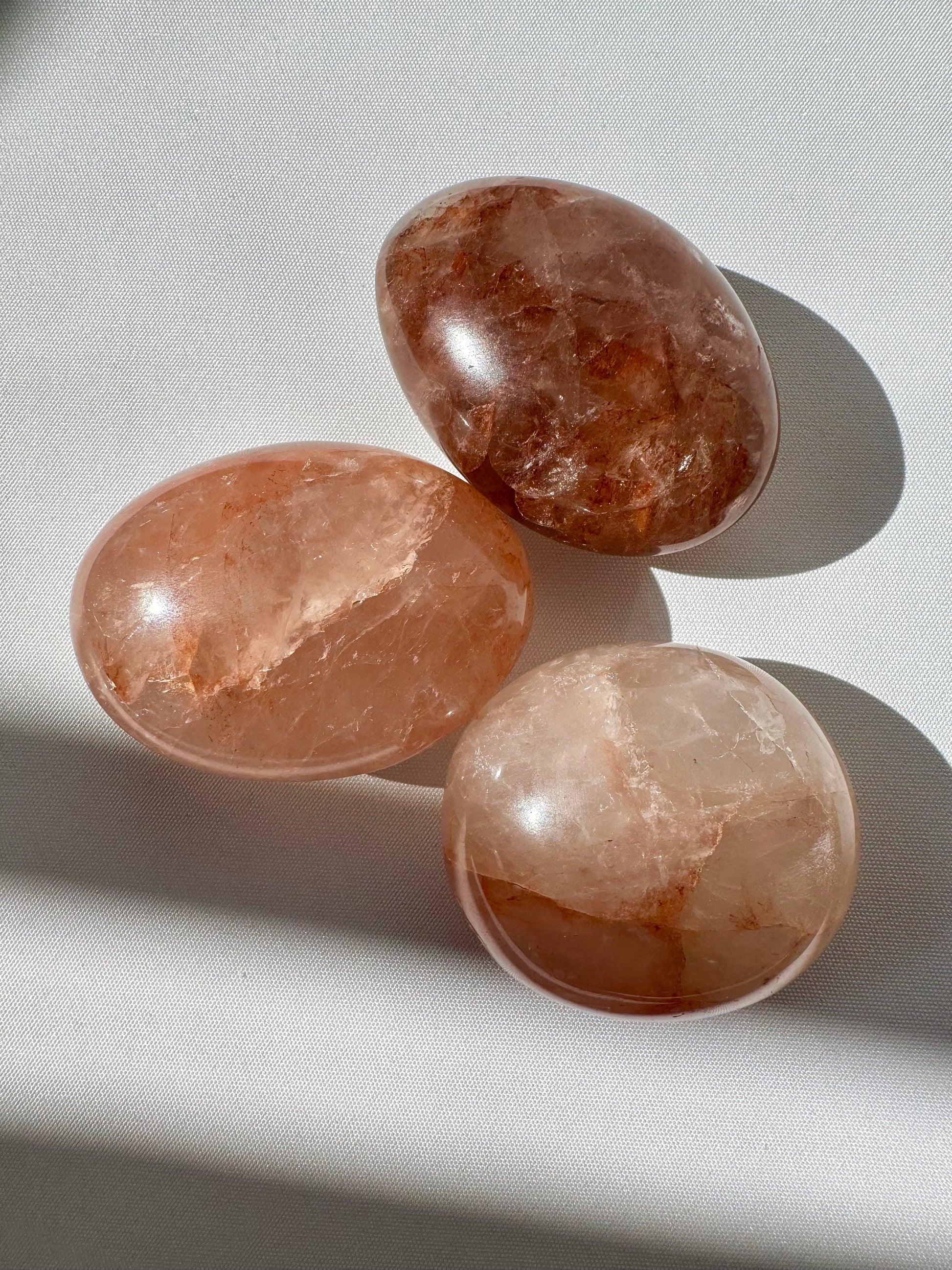 Set of three Fire Quartz Crystal Palm Stones with fiery red and orange hues on white fabric, ideal for grounding and emotional healing.
