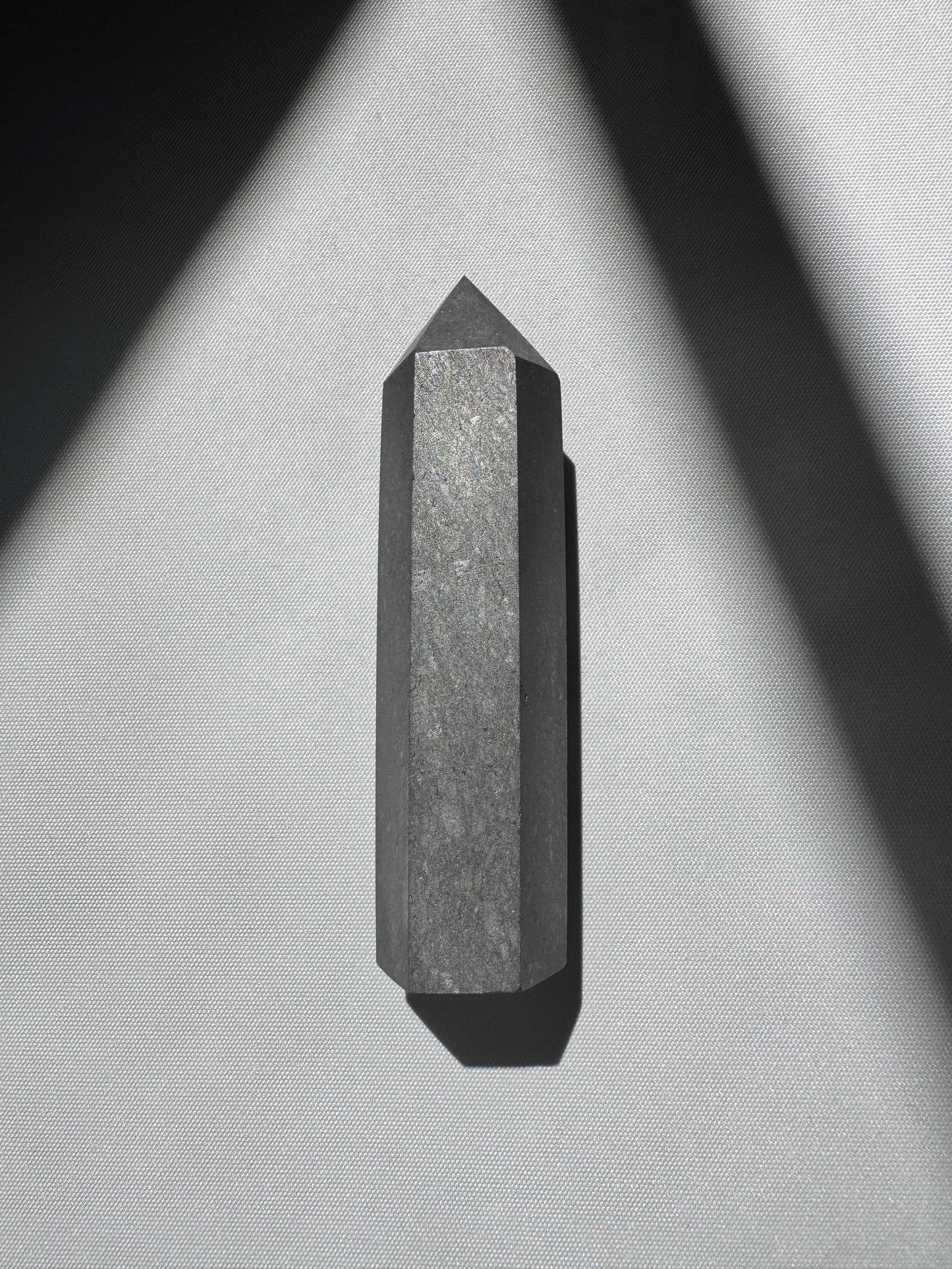 Top view of Shungite Crystal Point | Bespoke Crystals | emphasizing its smooth texture and symmetrical faceted edges.