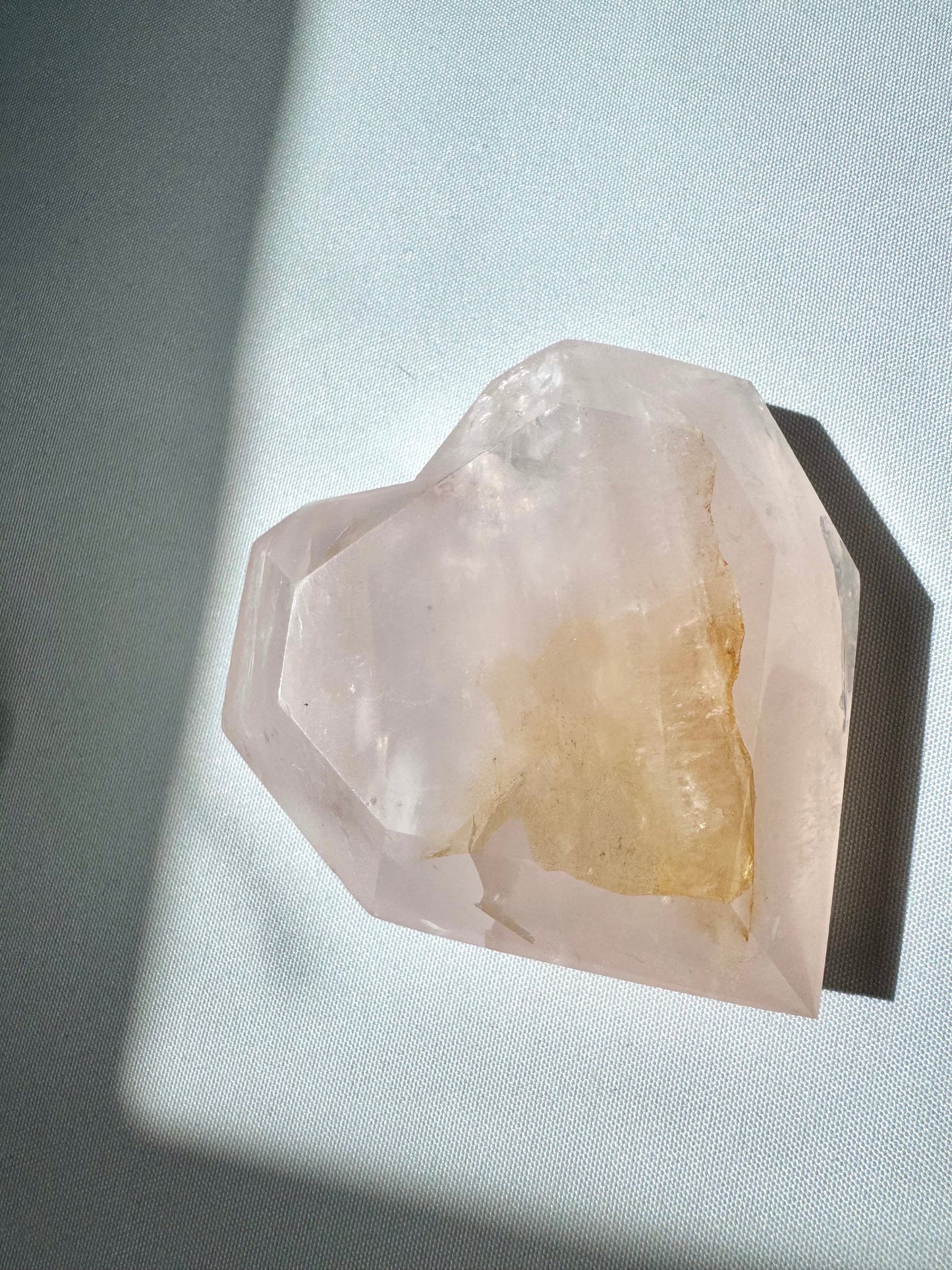 Bespoke Faceted Rose Quartz Crystal Heart featuring a visible Golden Healer inclusion, lying flat under natural sunlight.