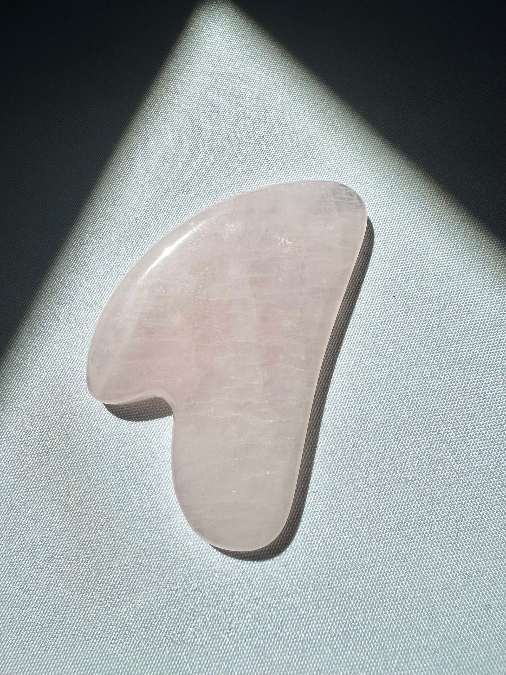 Single Rose Quartz Crystal Gua Sha by Bespoke Crystals on a white surface, showcasing its smooth texture and natural pink hue.