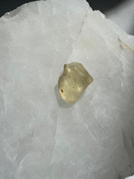 Libyan Desert Crystal Glass collectible with translucent yellow hue, displayed on a white mineral slab under natural light. Ideal for rock and fossil collectors.