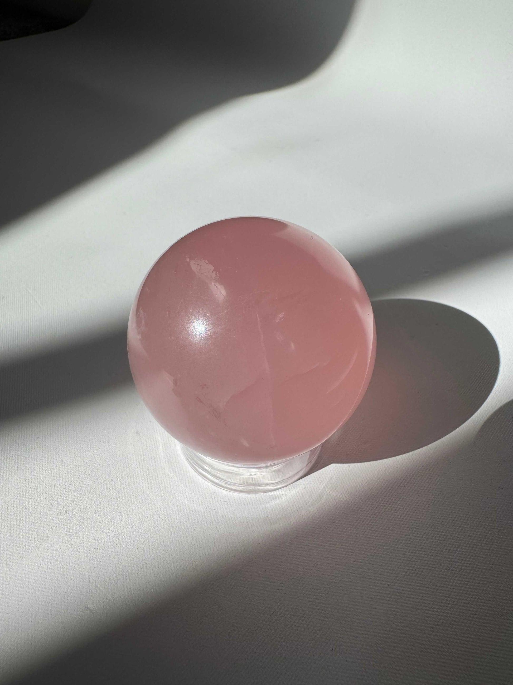 Shimmering Rose Quartz Crystal Star Sphere on clear stand, showcasing its natural beauty and metaphysical properties for peace and love.