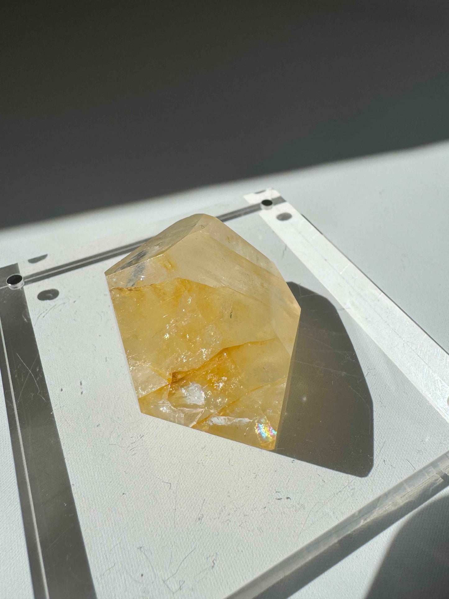 Golden Healer Crystal Freeform with radiant yellow hues and natural inclusions, displayed on a clear acrylic base under sunlight.