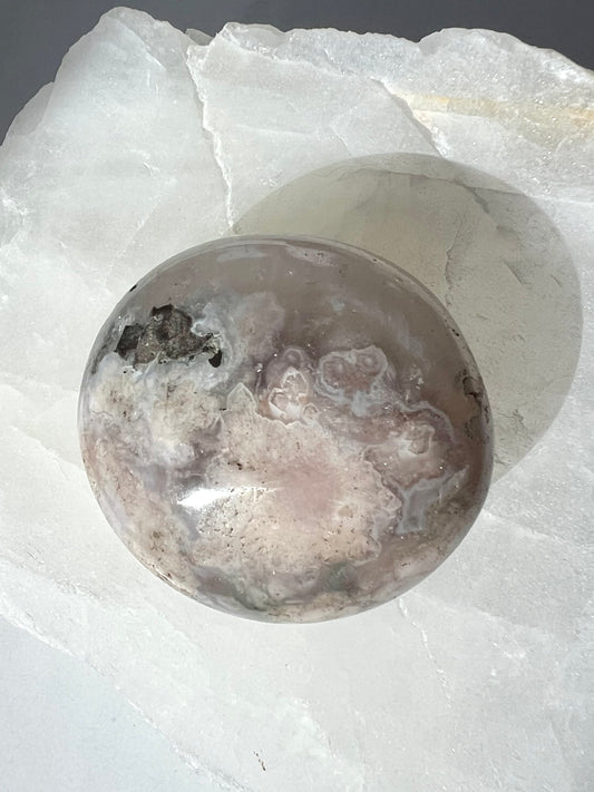 Polished Flower Agate Crystal Palm Stone with soft pink and white floral patterns, displayed on a white quartz slab. Ideal for healing and transformation | Healing Crystals and Gemstones New Zealand