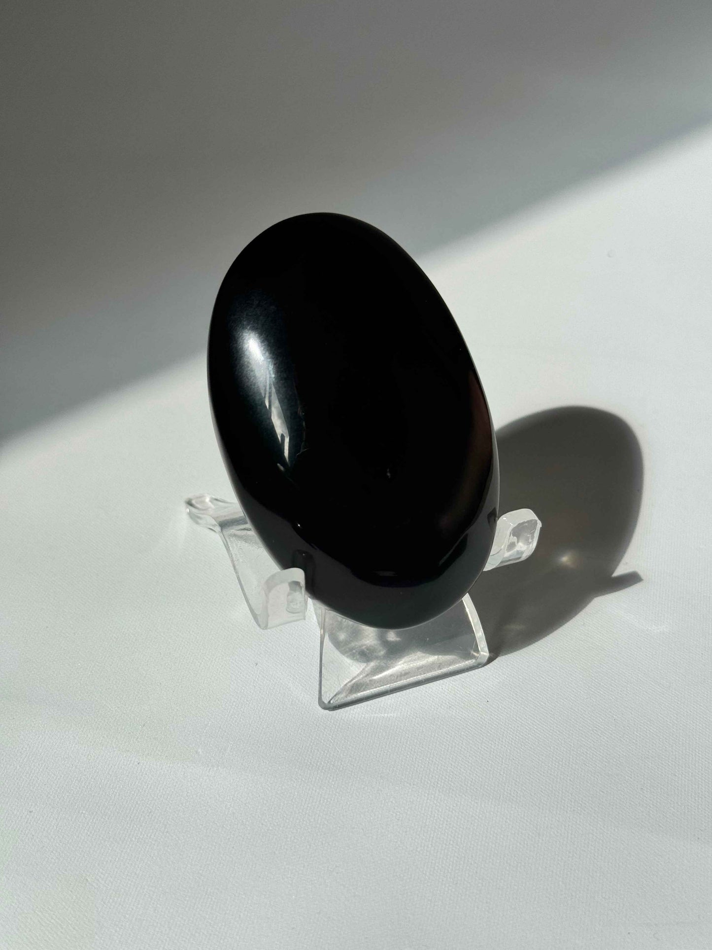 Single Rainbow Obsidian Crystal Palm Stone on a clear display stand, showcasing its smooth, glossy finish for bespoke crystal collections.