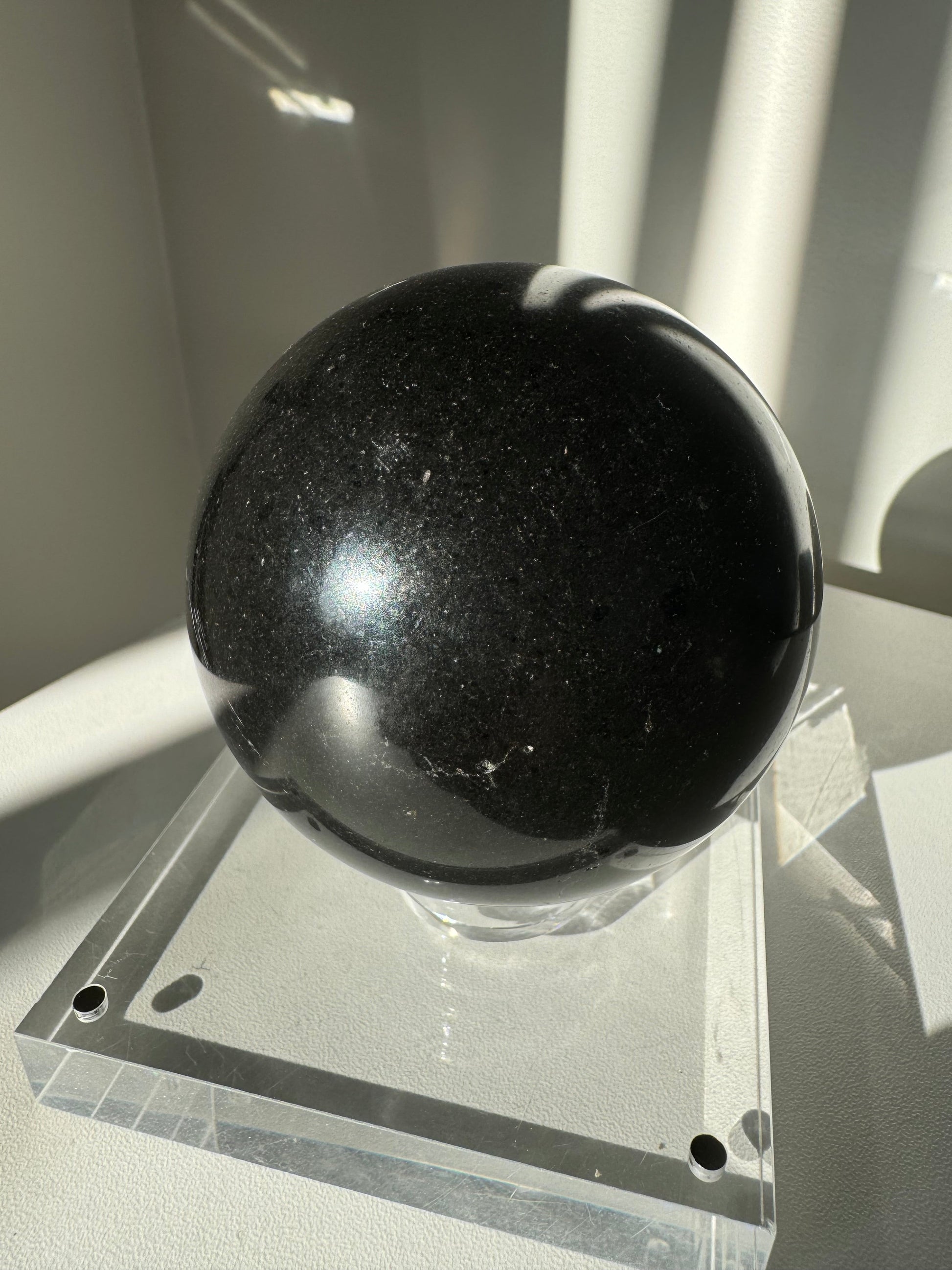 Black Tourmaline Crystal Sphere #3 on clear acrylic stand, ideal for protection and grounding in meditation or home decor.