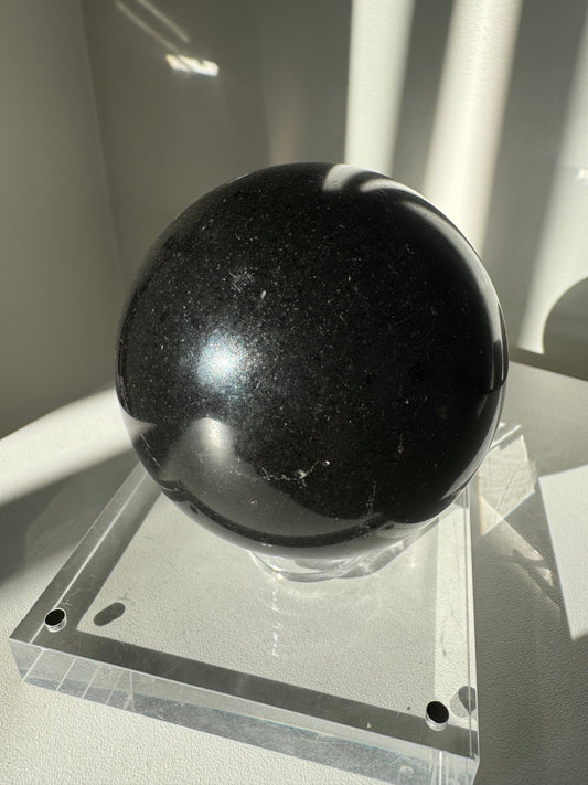 Black Tourmaline Crystal Sphere #3 on clear acrylic stand, ideal for protection and grounding in meditation or home decor.