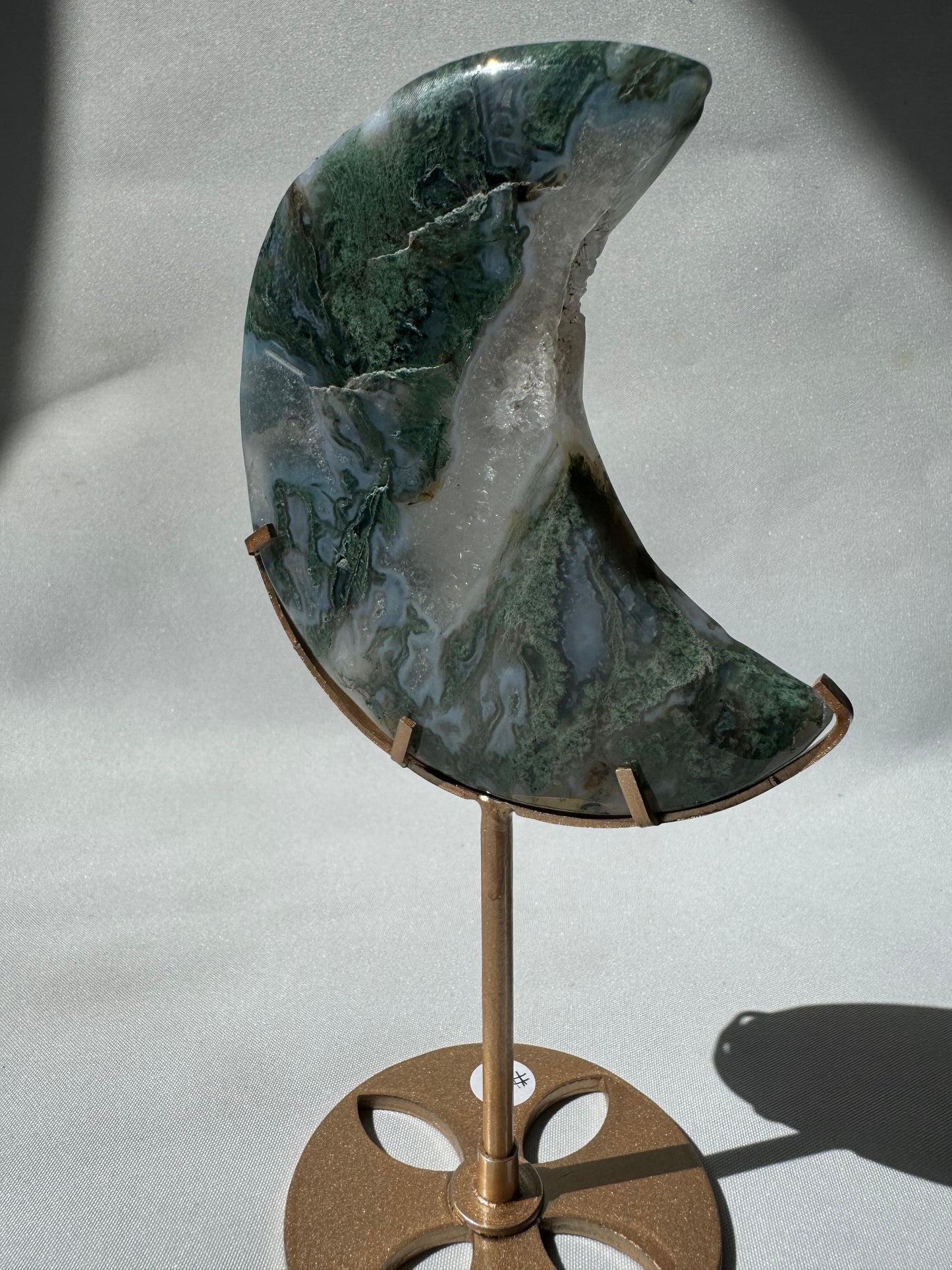 Side view of Moss Agate Crystal Moon on Stand #1 showing natural green patterns and shimmering druzy surface on a sleek gold base.