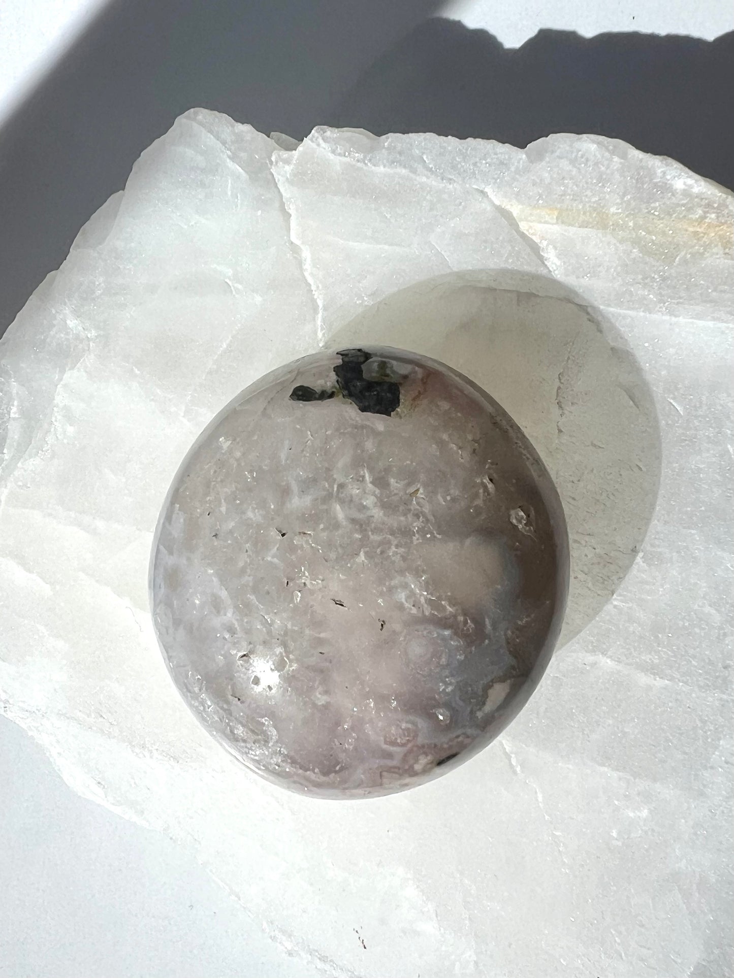 Round Flower Agate Palm Stone featuring ethereal hues and natural inclusions, resting on a translucent white crystal base. Perfect for collectors and crystal lovers | Bespoke Crystals Auckland