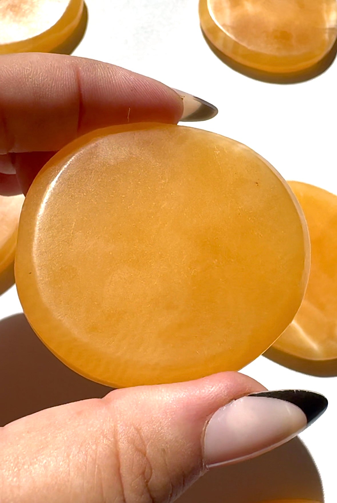 Close-up of a hand holding an Orange Calcite Crystal Sun Disc | Bespoke Crystals, emphasizing its polished surface and vibrant orange hue.