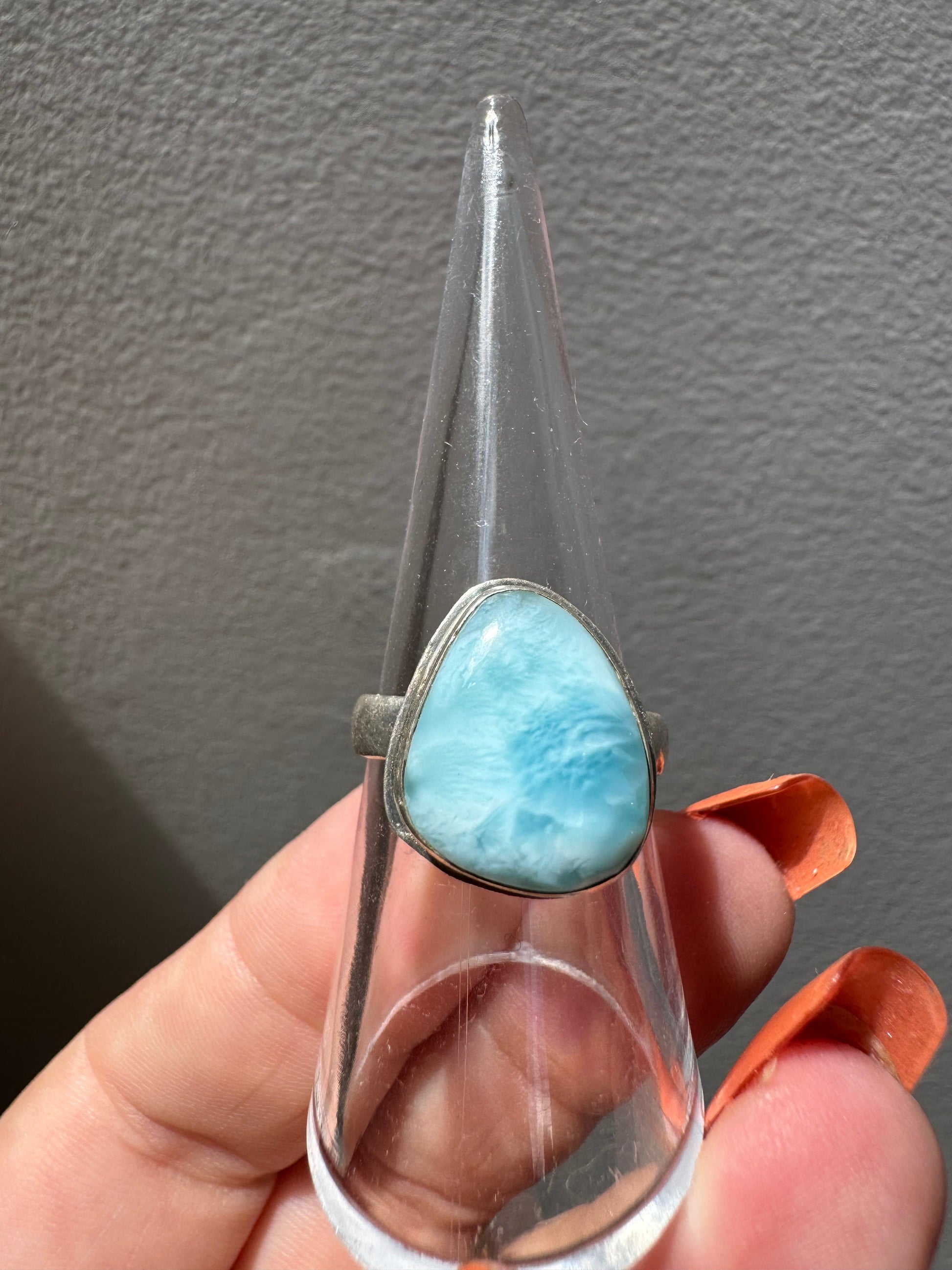 Larimar Crystal Ring #2 | Bespoke Crystals featuring a teardrop-shaped sea-blue Larimar stone set in a silver band, displayed on a clear ring stand.