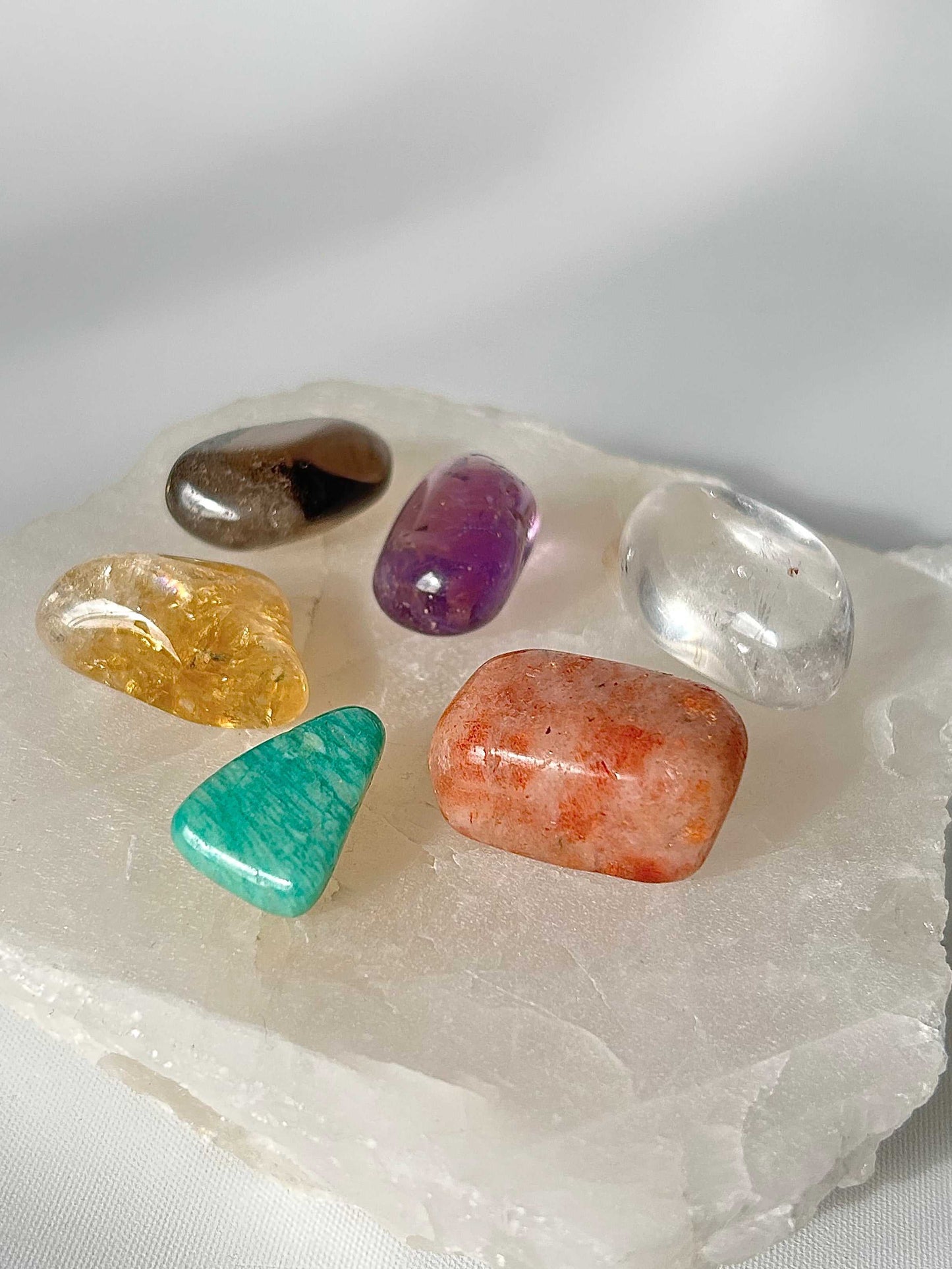 Crystal Healing Essentials set with vibrant tumble stones like Sunstone, Smoky Quartz, and Quartz displayed on a selenite slab for energy balance.