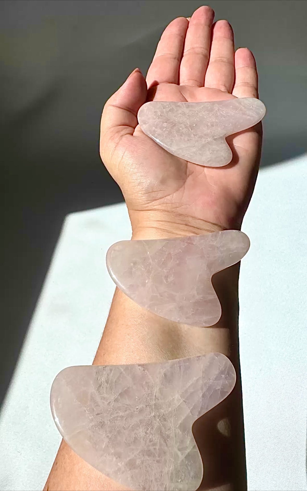 Hand holding and displaying three Rose Quartz Crystal Gua Sha tools from Bespoke Crystals, ideal for facial massage and skincare routines.