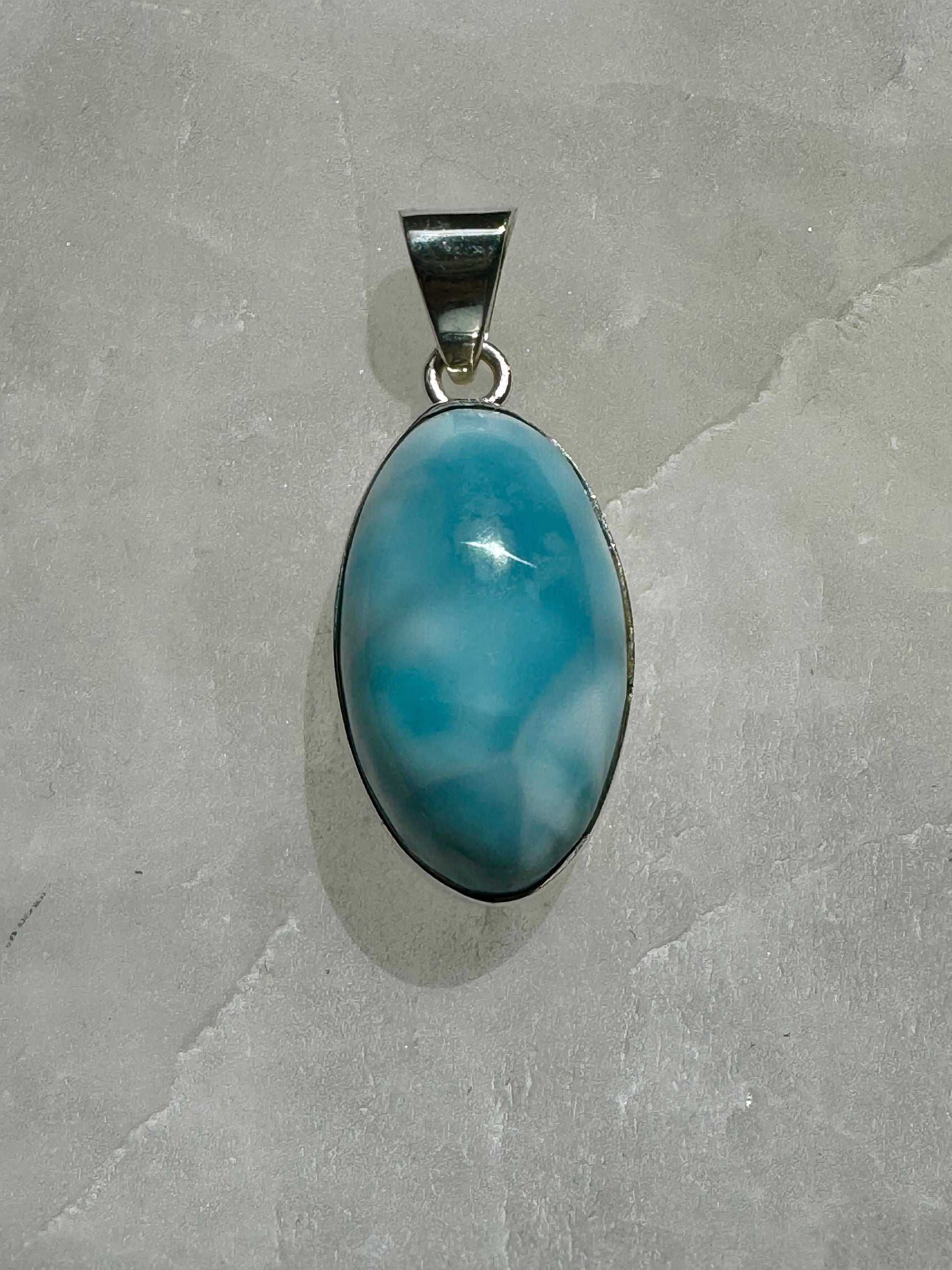 Oval-shaped Larimar Crystal Pendant set in 925 sterling silver, showcasing its calming blue hues on a grey stone surface | Bespoke Crystals NZ