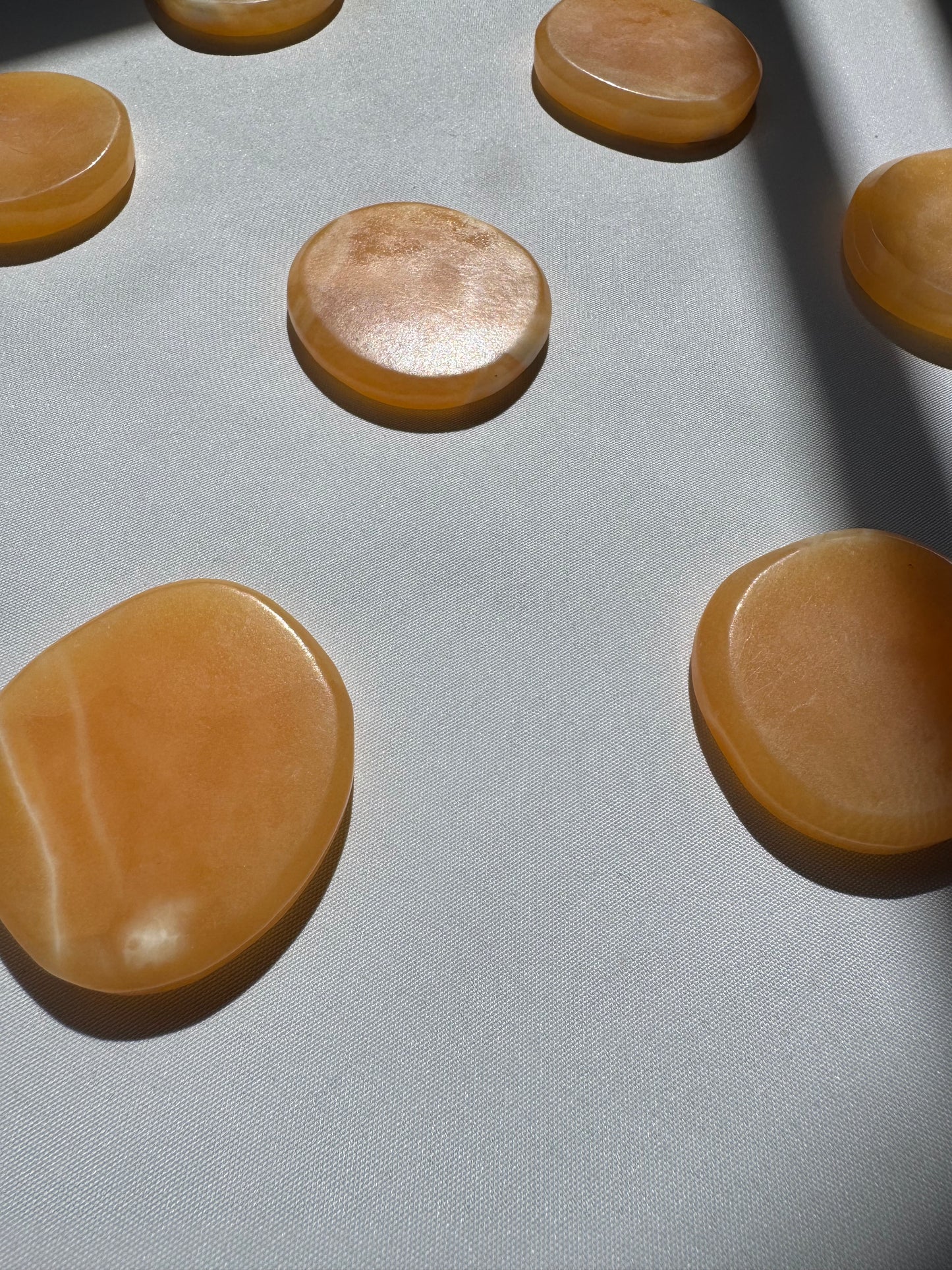 Orange Calcite Crystal Sun Discs | Bespoke Crystals displayed on white fabric, showcasing their smooth, polished finish and warm amber tones.