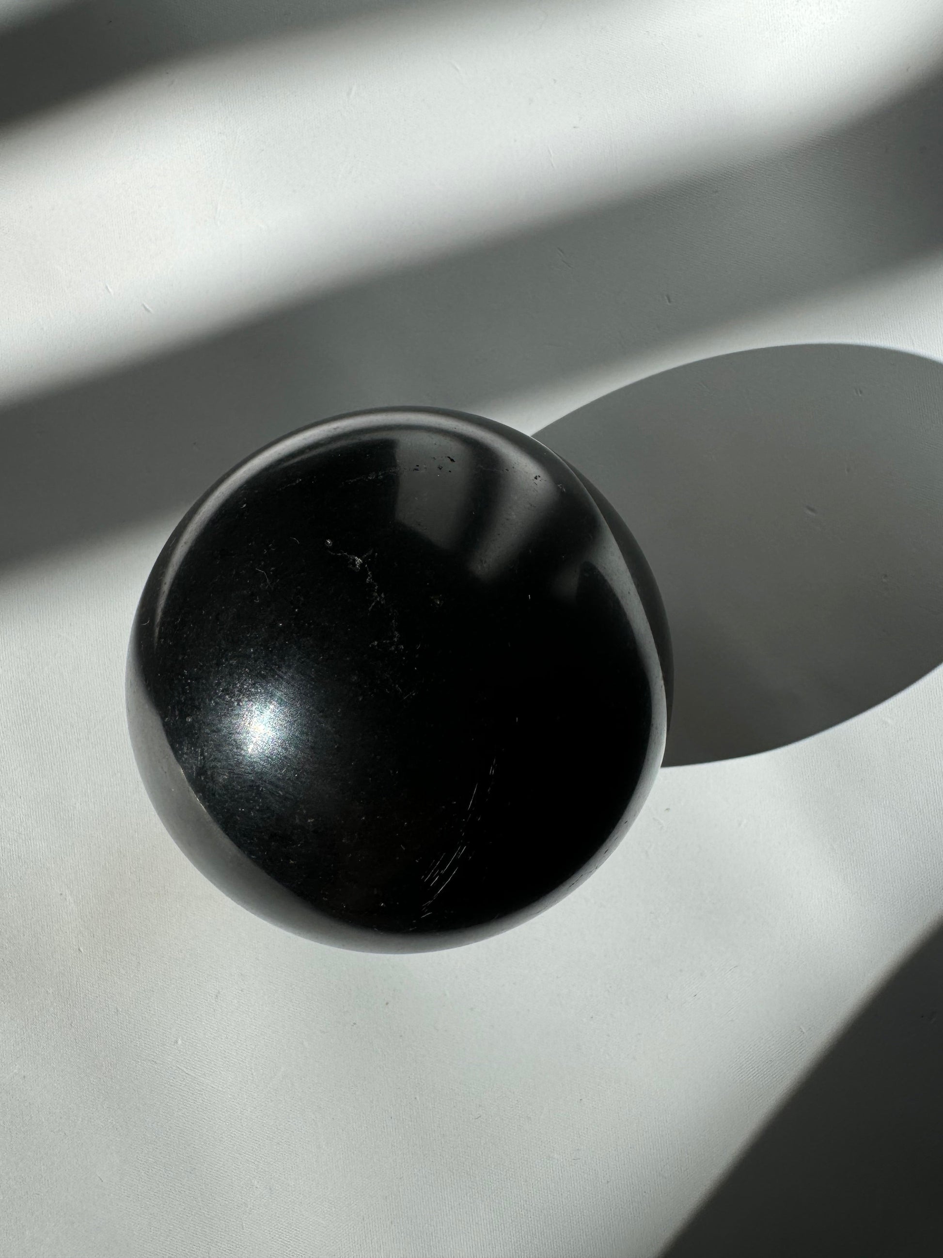 Polished Black Tourmaline Crystal Sphere #3 casting a shadow on white surface, perfect for spiritual cleansing and energy shielding.