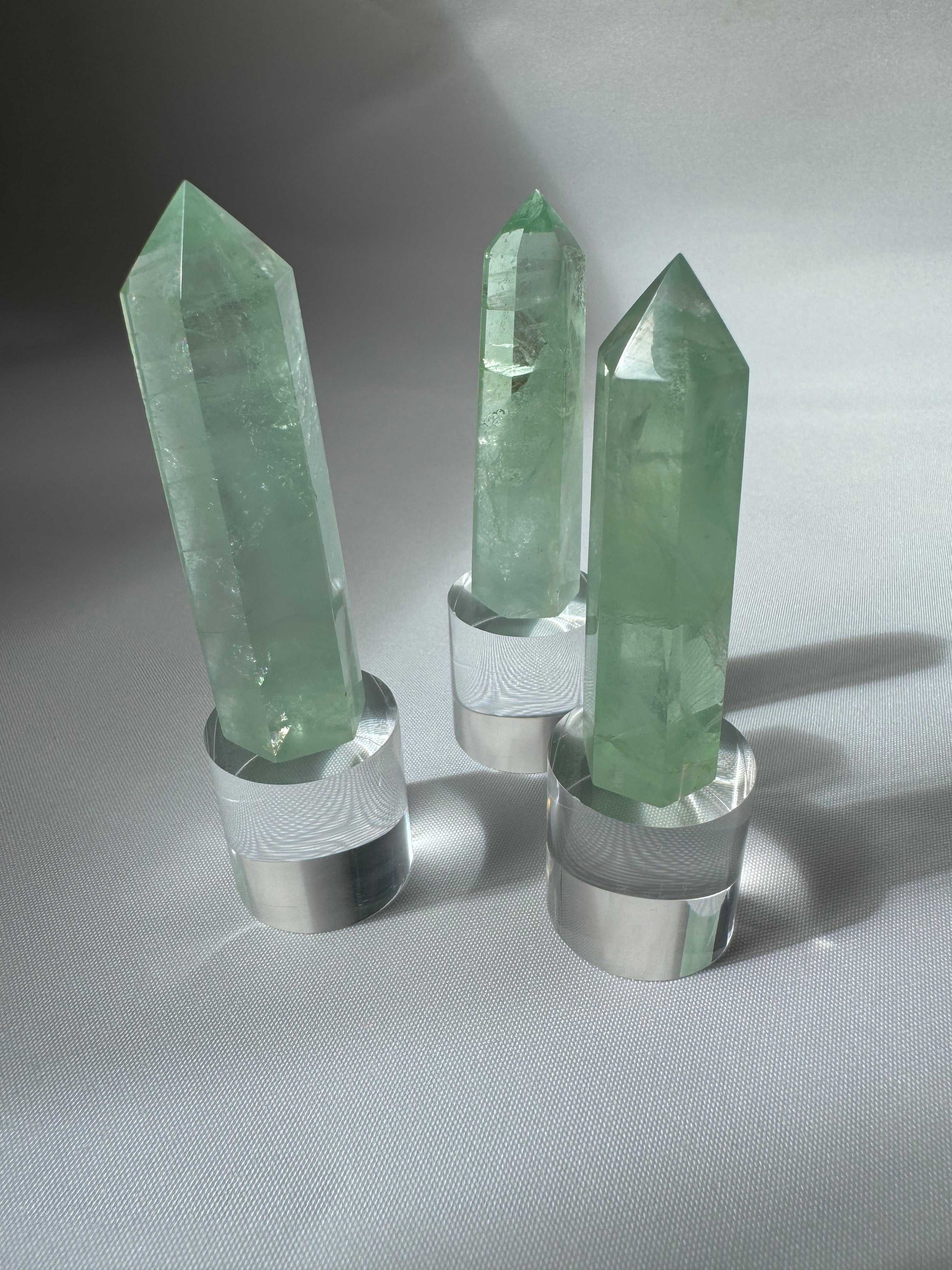 Three Green Fluorite Crystal Points standing on clear acrylic bases, perfect for display or use in wellness rituals and bespoke crystal collections.