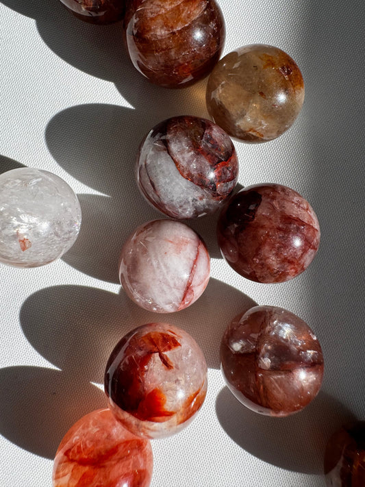 Mini Fire Quartz Crystal Spheres with red and gold iron oxide inclusions on white background, ideal for grounding and protection rituals.