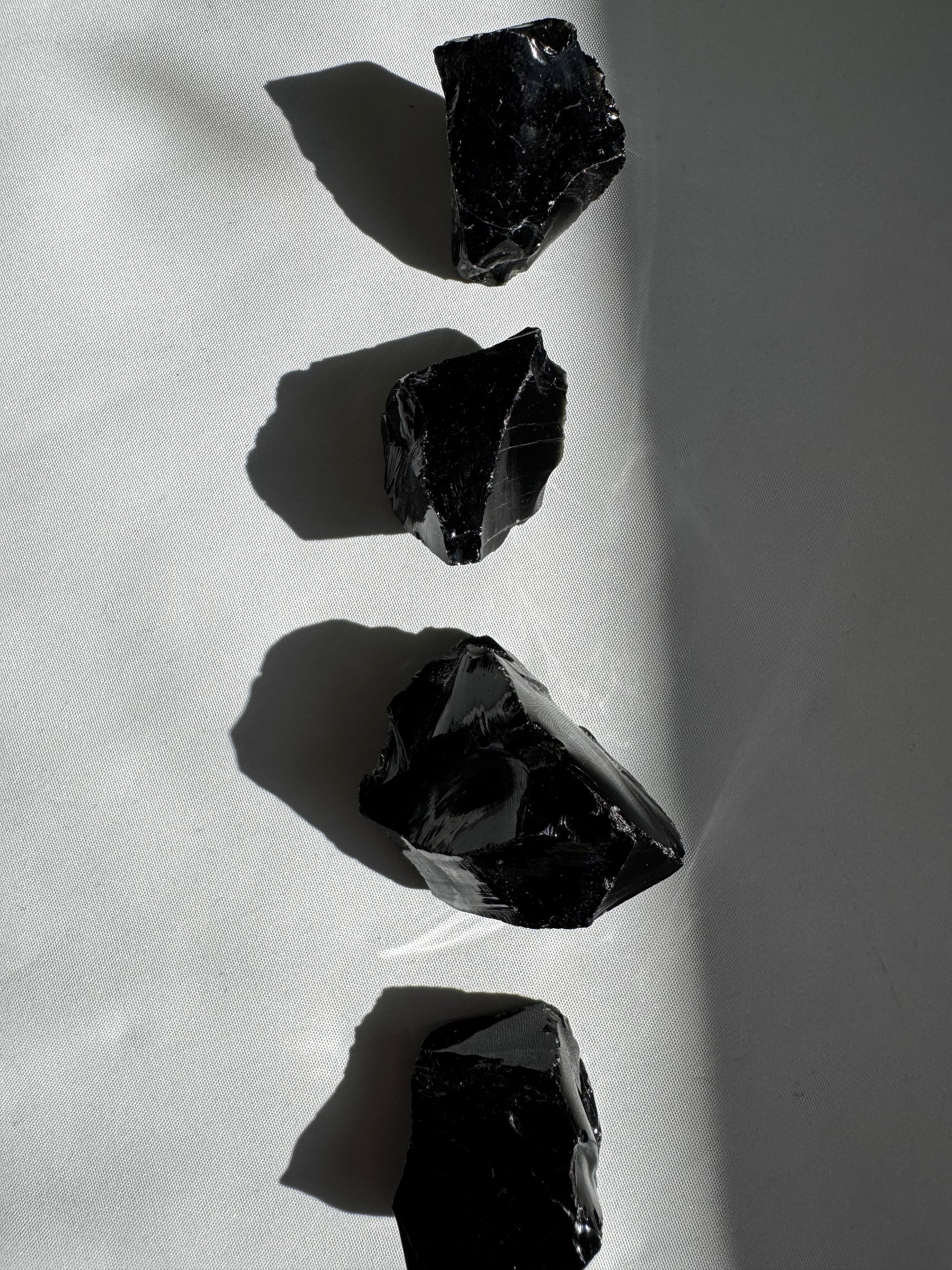 Black Obsidian Crystal Rough Piece | Bespoke Crystals aligned in natural light, highlighting the raw texture and deep black sheen of each volcanic glass piece.