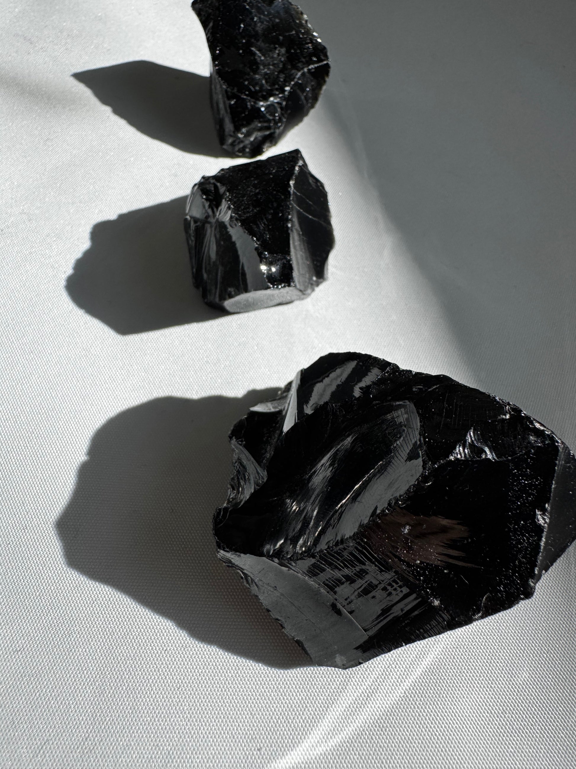 Black Obsidian Crystal Rough Piece | Bespoke Crystals showcasing raw, reflective black stones arranged on a white surface for collectors and healers.
