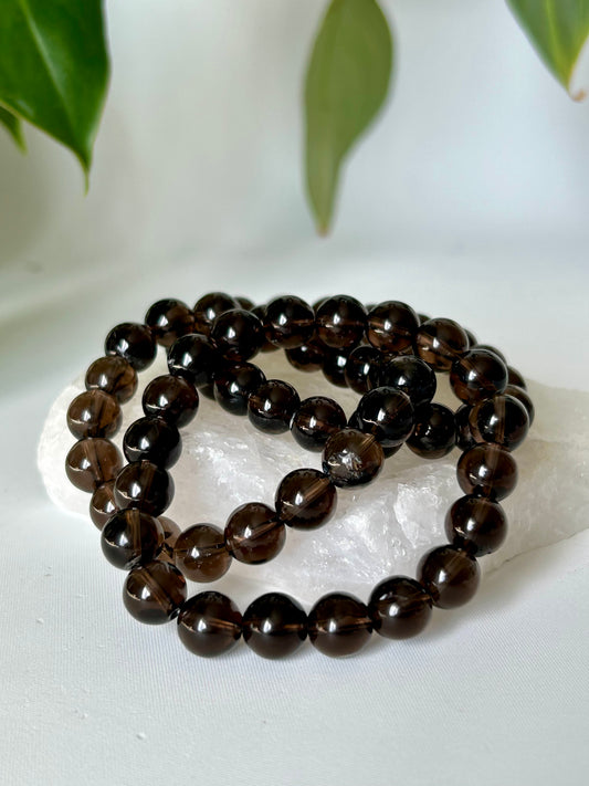 Smokey Quartz Bracelet 10mm with polished round beads, displayed on a white crystal slab for grounding and protection energy.