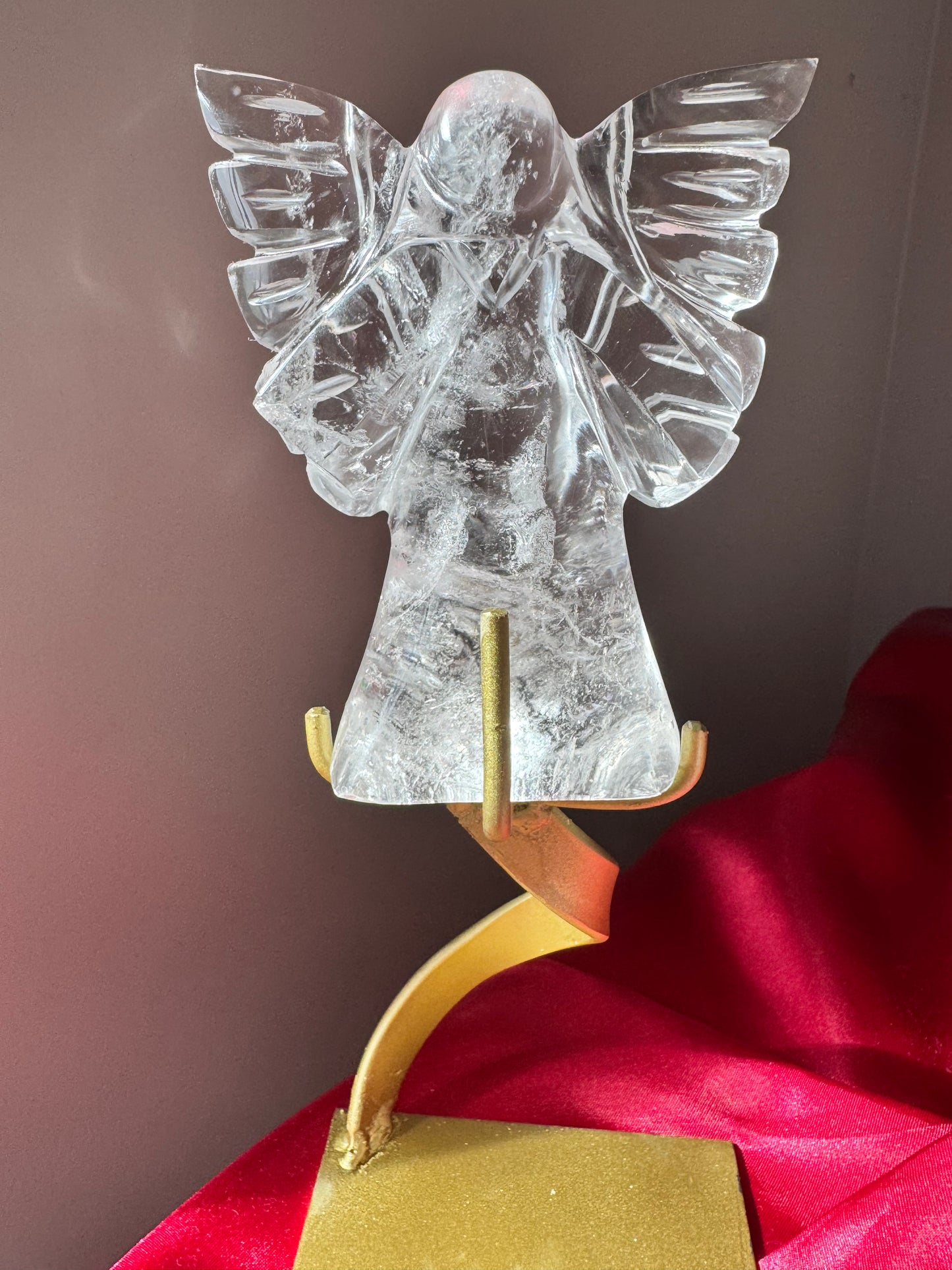Quartz Angel - Celestial Hand Carved figurine displayed on a gold stand, shimmering with clarity against a red velvet background.
