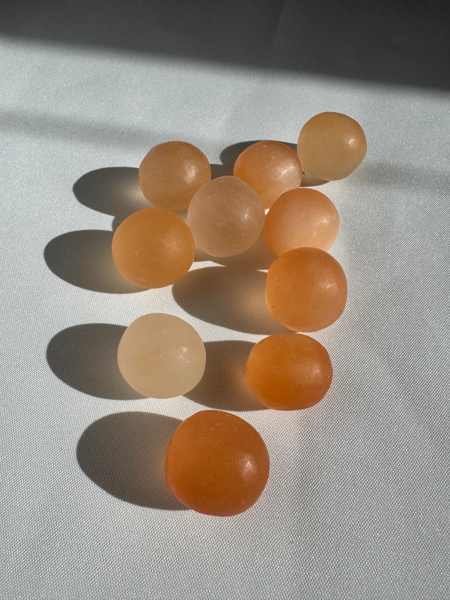 Set of Orange Satin Spar Tumble Stones ideal for stress relief and spiritual wellness, arranged in soft sunlight.