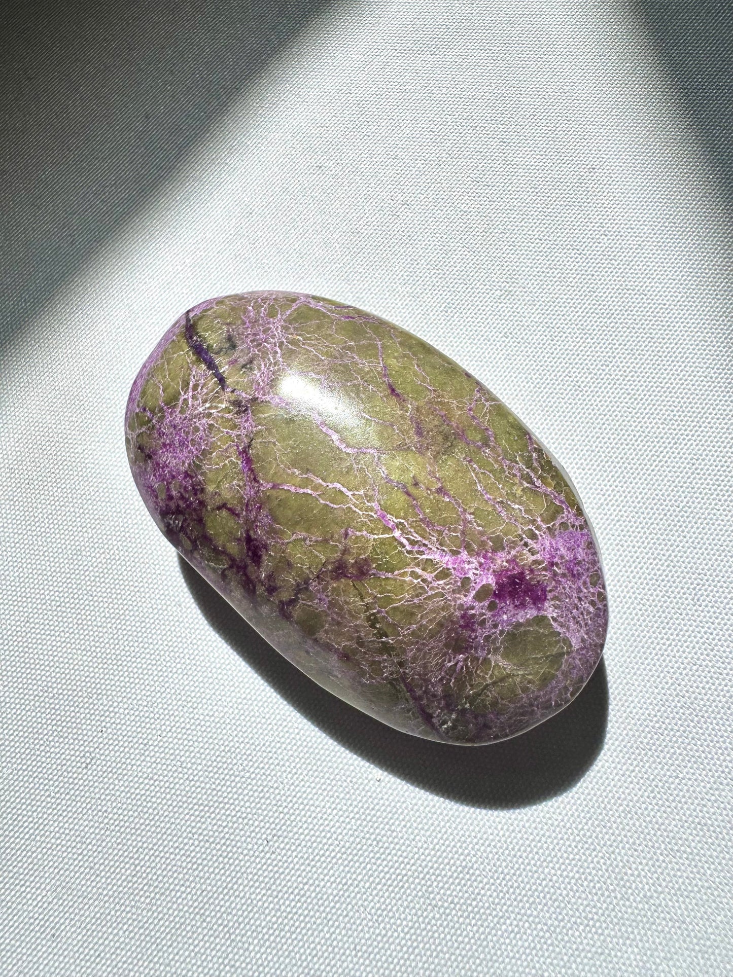 Polished Atlantisite Crystal Palm Stone featuring vivid green serpentine and purple stichtite patterns, ideal for emotional healing rituals.